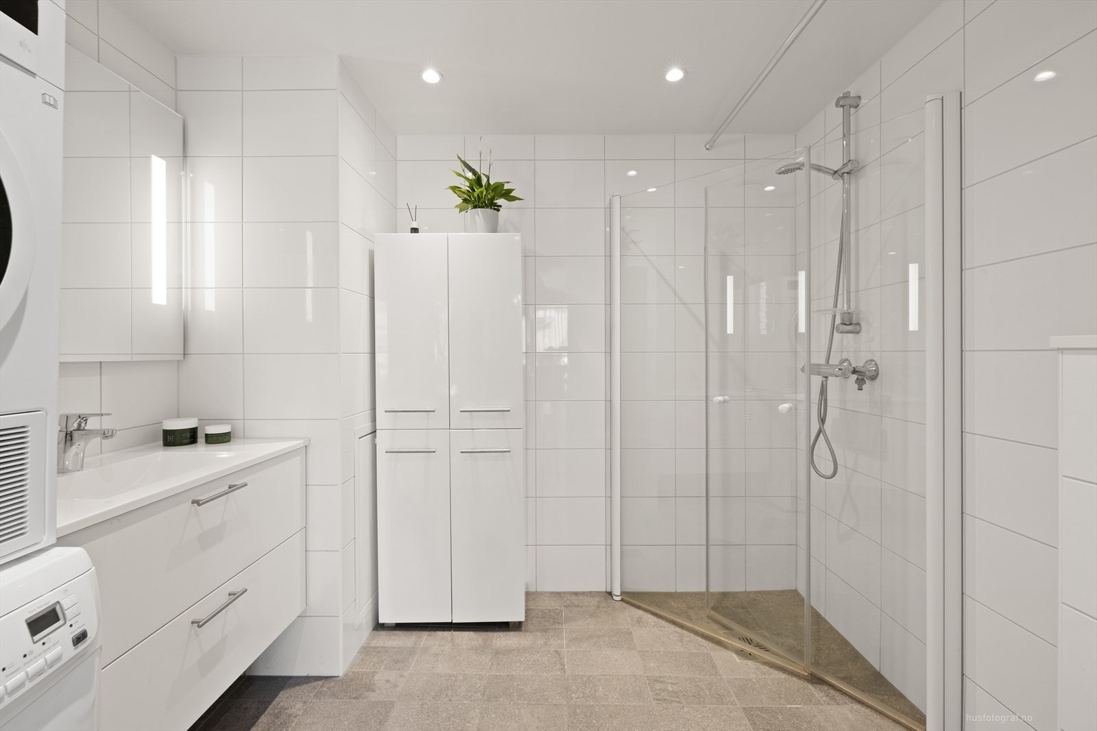 Badet er praktisk innredet med vegghengt toalett, servant på skuffeseksjon, dusjhjørne og høyskap. Galleribilde