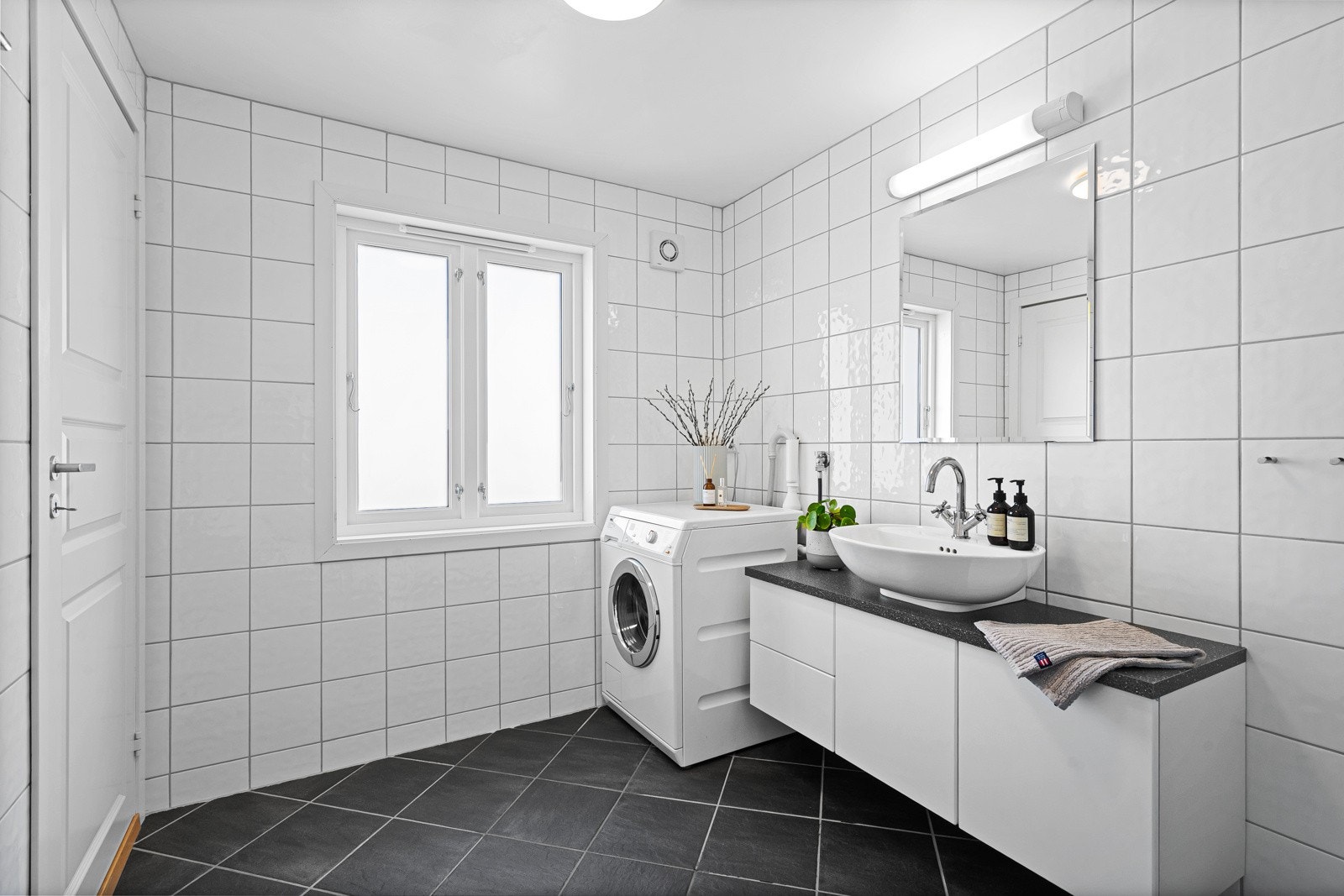 Helfliset bad med stilrent baderomsmøblement og opplegg for vaskemaskin. Galleribilde