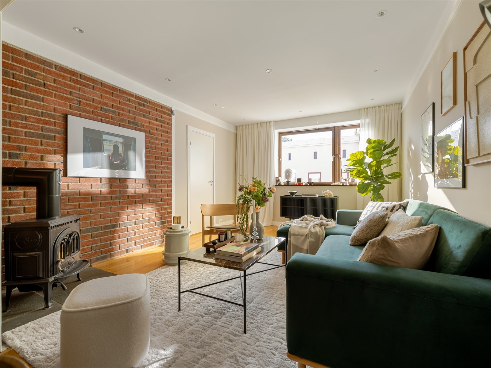 I midten av stuen står en pen vedovn som gir ekstra varme og hygge på kaldere dager. Teglsteinsveggen bak er en fin detalj i rommet. Galleribilde