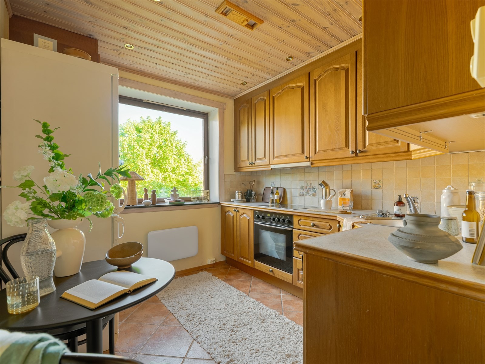 Romslig kjøkken med malte vegger, trepanel i tak og flislagt gulv, samt godt med innlys fra stort vindu. Galleribilde