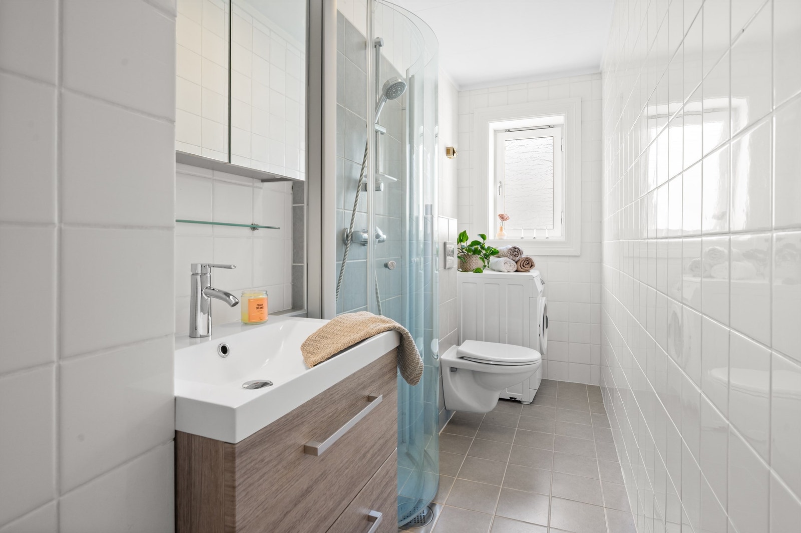 Badet er pent flislagt på gulv og vegger med varme i gulvet. Baderomsinnredningen består av vegghengt klosett, servant og dusjhørne. Over servanten er det et fint speil. Galleribilde