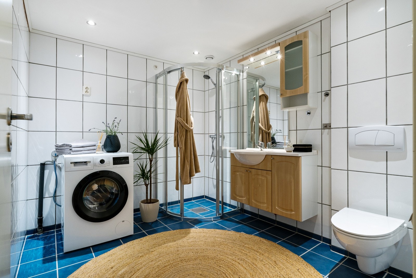 Baderommet måler 6,3 kvm og er innredet med opplegg for vaskemaskin, dusjhjørne, vegghengt toalett og en praktisk baderomsinnredning med servant. Galleribilde