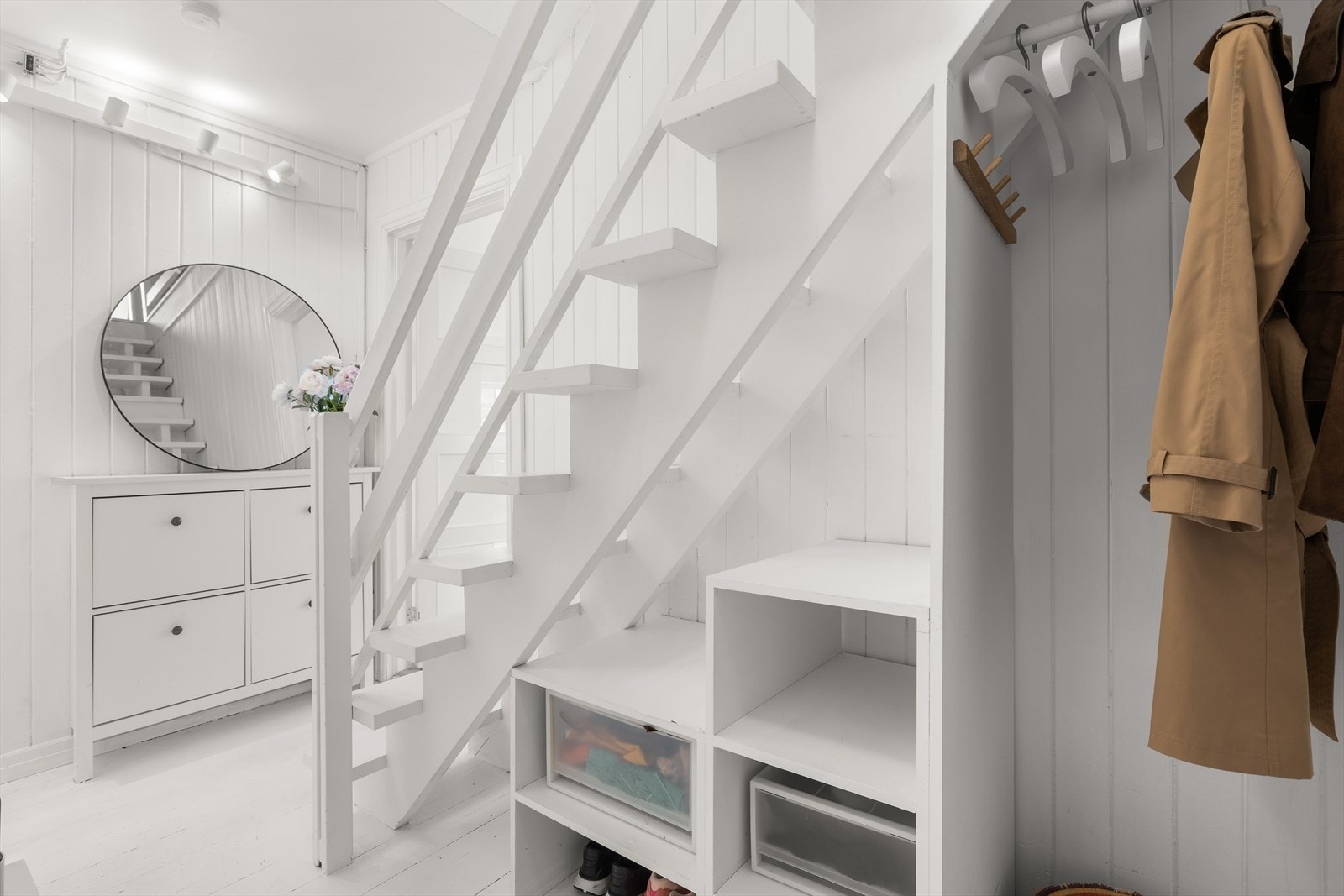 Den hvite fargen på både vegger og gulv gir rommet et luftig preg, og de smarte oppbevaringsløsningene under trappen gir god plass til sko og annet tilbehør. Galleribilde