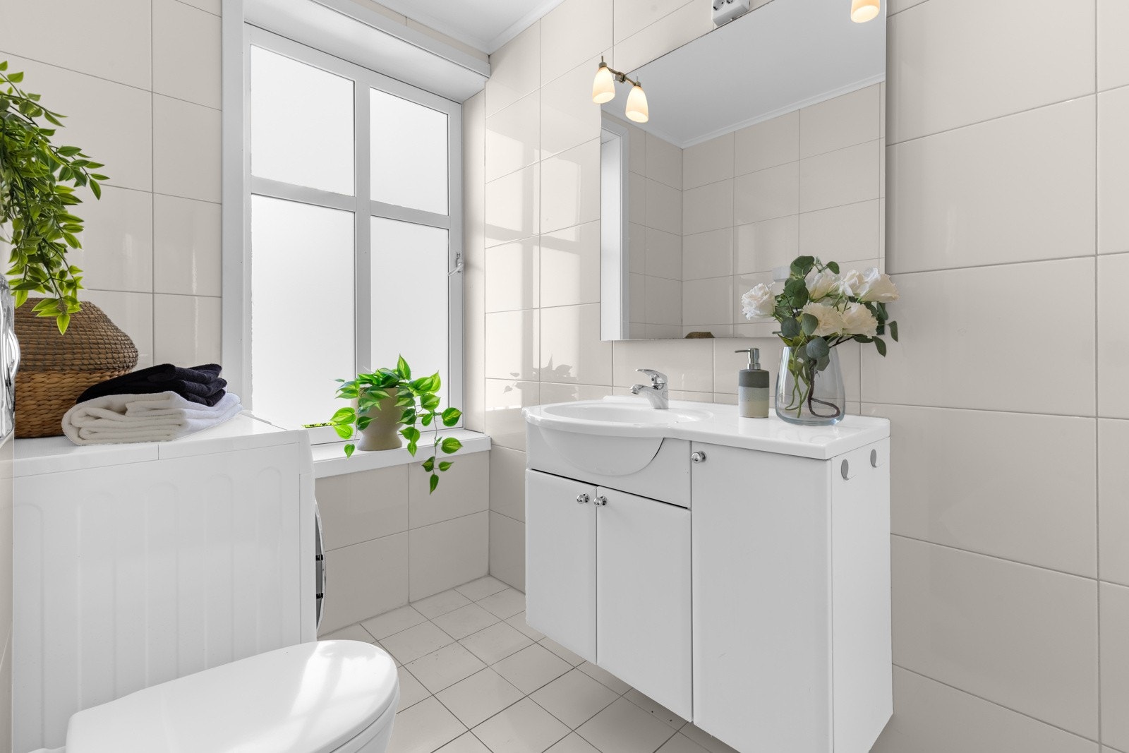 Baderommet inneholder servant med underskap, speil med overbelysning, vegghengt toalett og dusjhjørne. Galleribilde