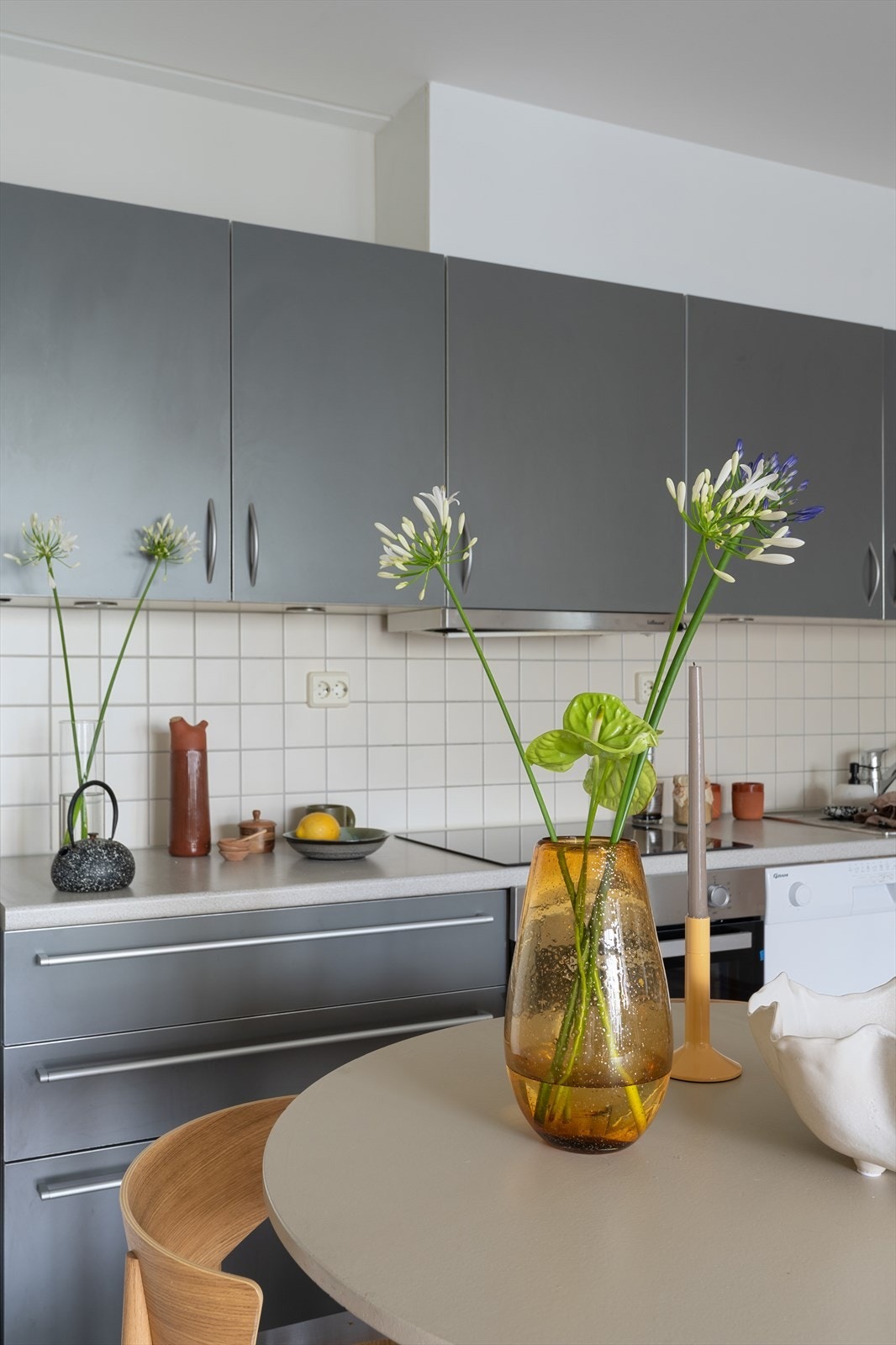 Kjøkkeninnredning med slette fronter, overskap med benkebelysning og fliser på vegg. Lys laminat benkeplate med nedfelt stålkum og ett-greps armaturer i krom. Galleribilde