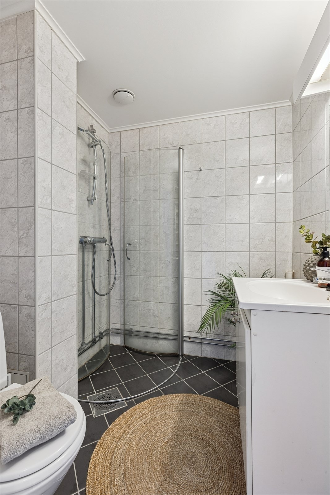 Baderommet har flislagte overflater, gulvvarme for ekstra komfort og praktisk dusjhjørne med buede svingdører. Innredning med heldekkende servant og speil med lysarmatur. Galleribilde