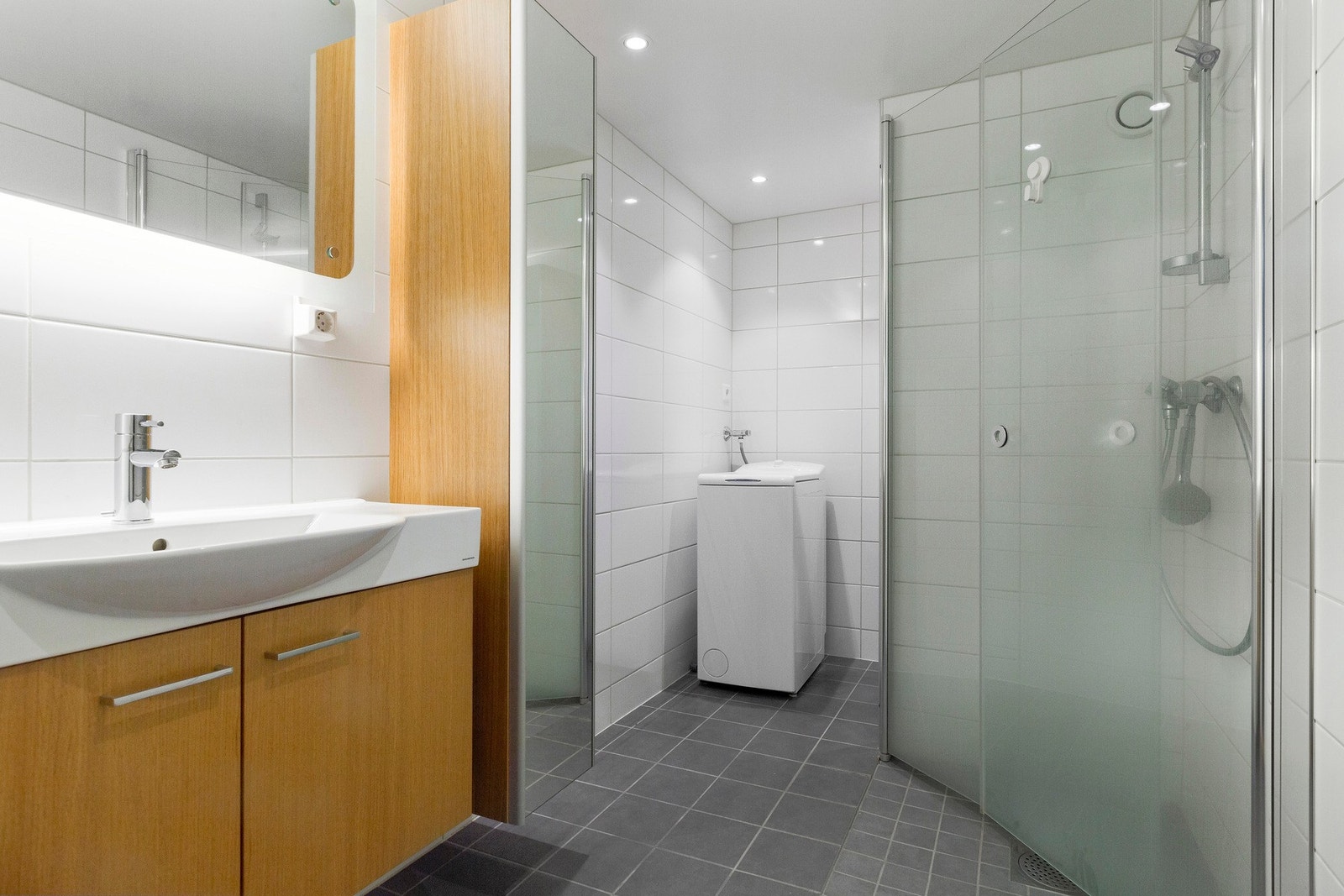 Moderne flislagt bad med opplegg for vaskemaskin, varme i gulv, downlights i tak og innfellbare dusjedører i glass. Galleribilde