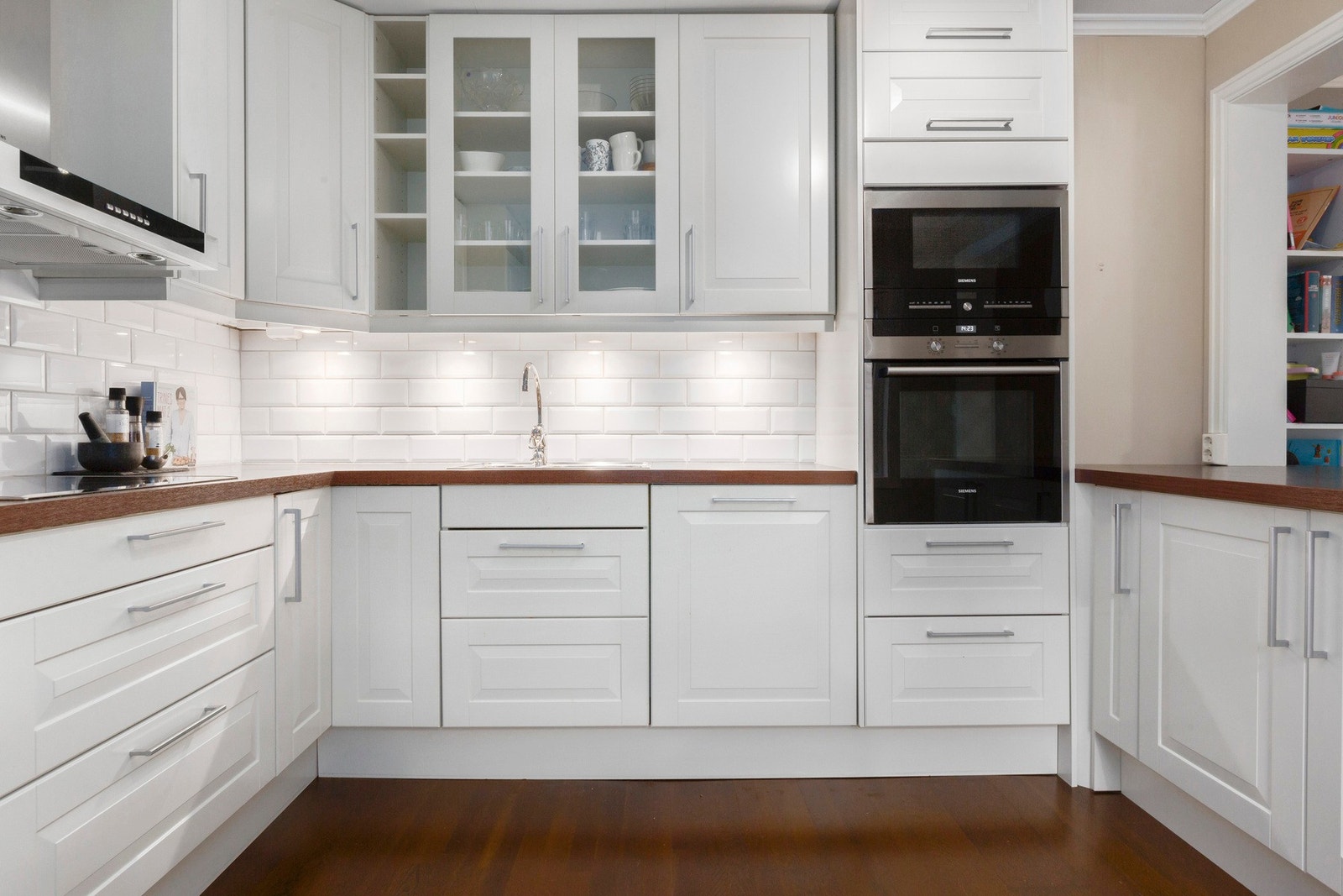 Et romslig kjøkken med pene hvite fronter, tidløse fliser mellom benkeplate og takhøyde-overskap. Godt med oppbevaringsplass. Galleribilde