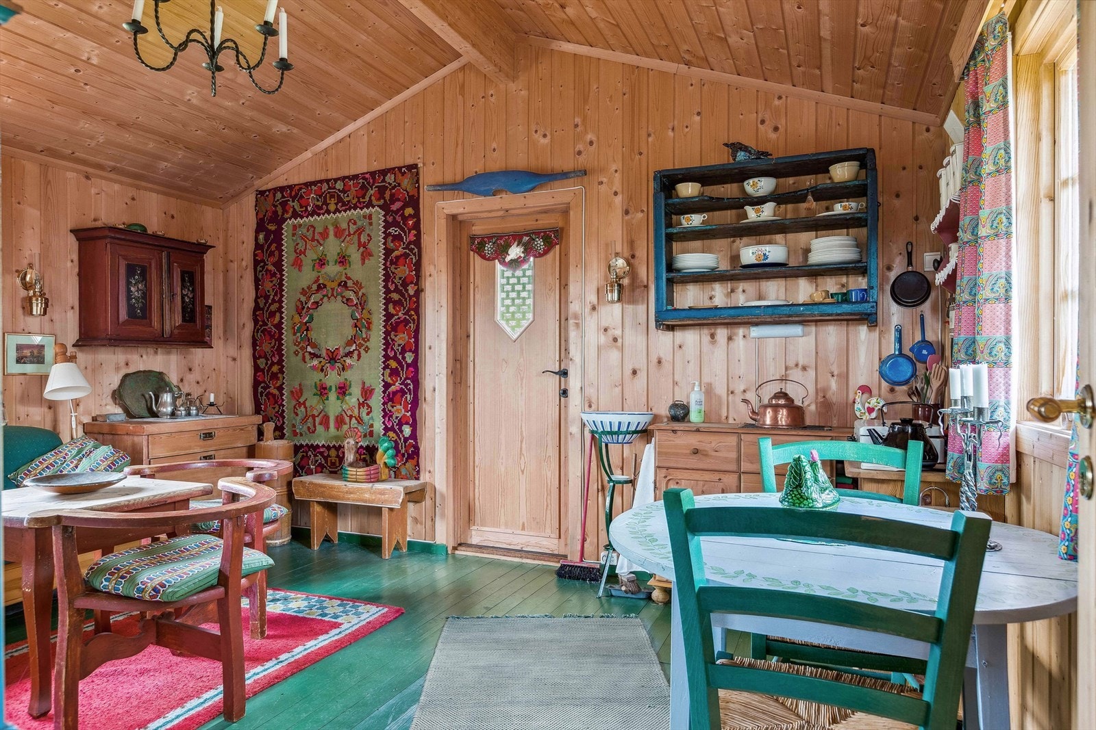 Inne i annekset er det et hyggelig oppholdsrom hvor en hvitmalt elementpeis med innsyn gir lun og god varme til rommet. Galleribilde