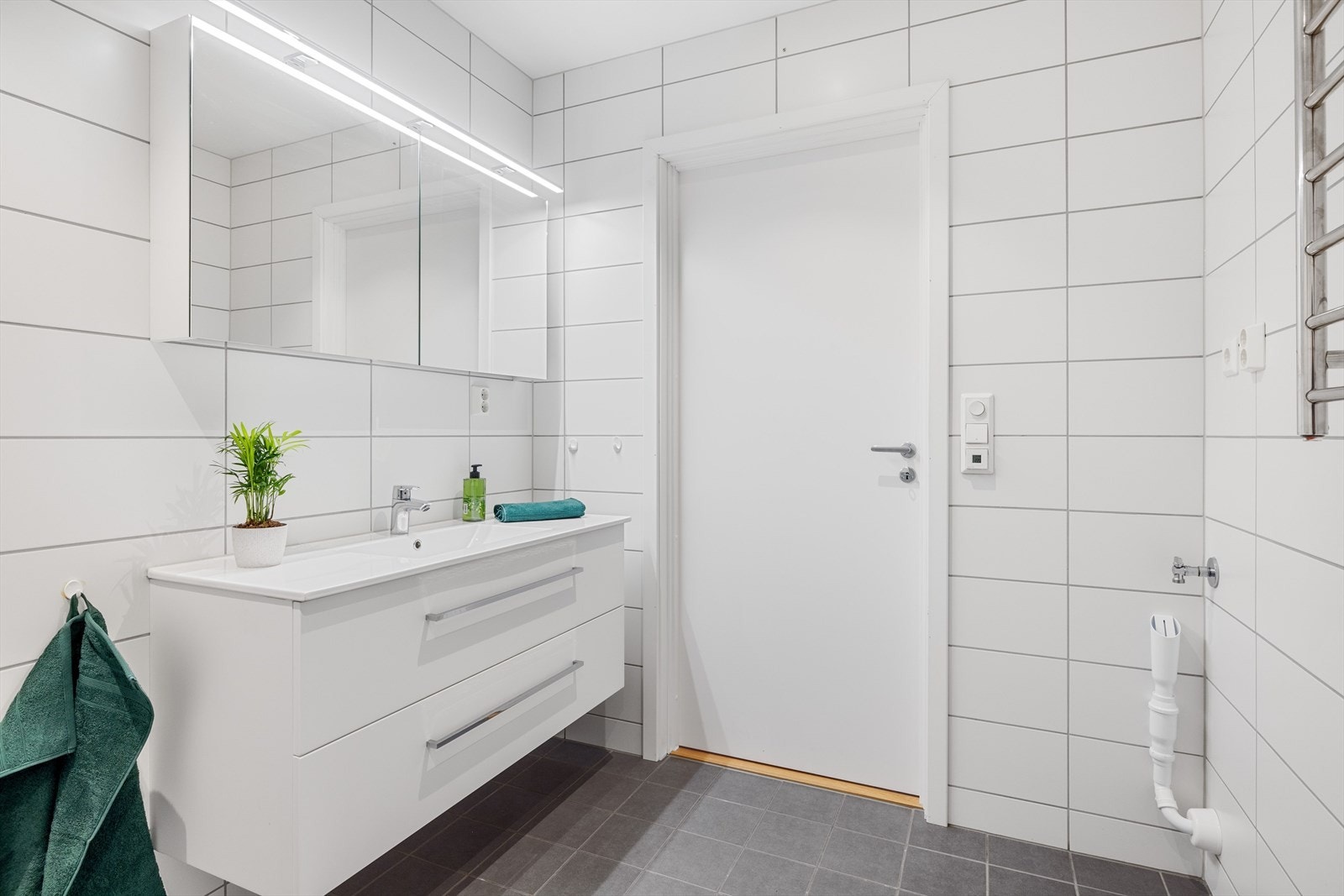 I hjørnet er det plass og opplegg for vaskemaskin og tørketrommel over om ønskelig. Baderommet er også utstyrt med dusjhjørne med innfellbare glassdører og vegghengt toalett. Galleribilde