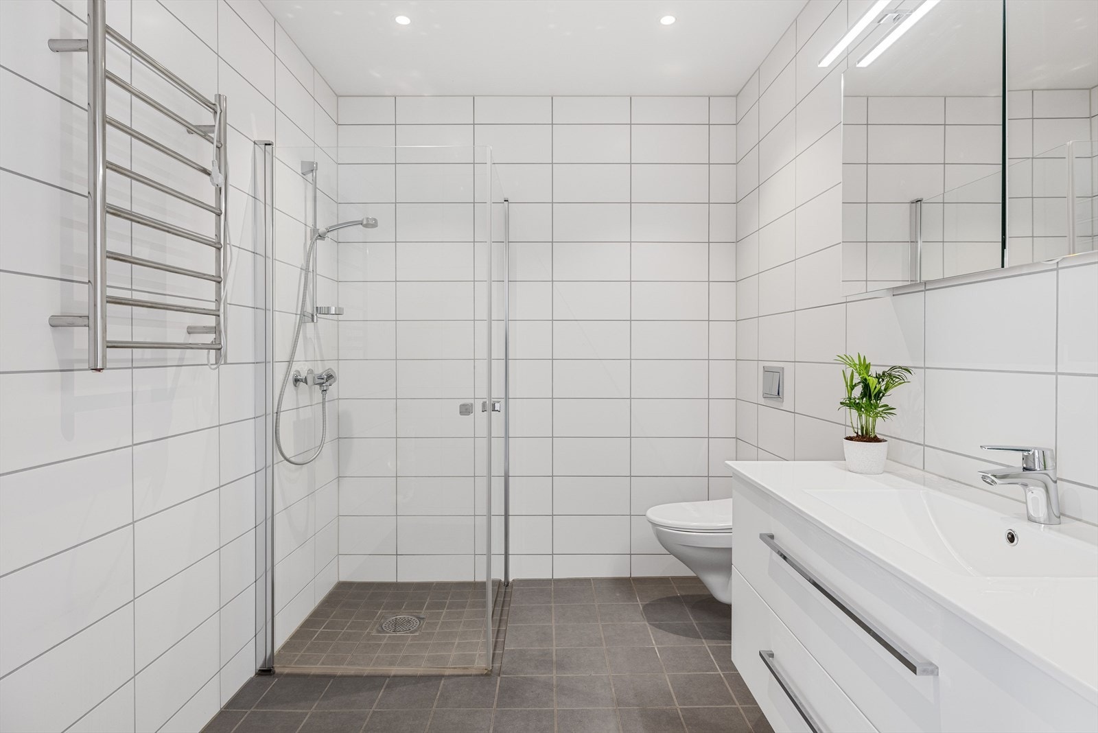 Boligen har et lyst og moderne baderom fra byggeåret 2020. Baderommet har grå fliser på gulv med gulvvarme, hvite fliser på veggene, downlights i himlingen og balansert ventilasjon. Galleribilde