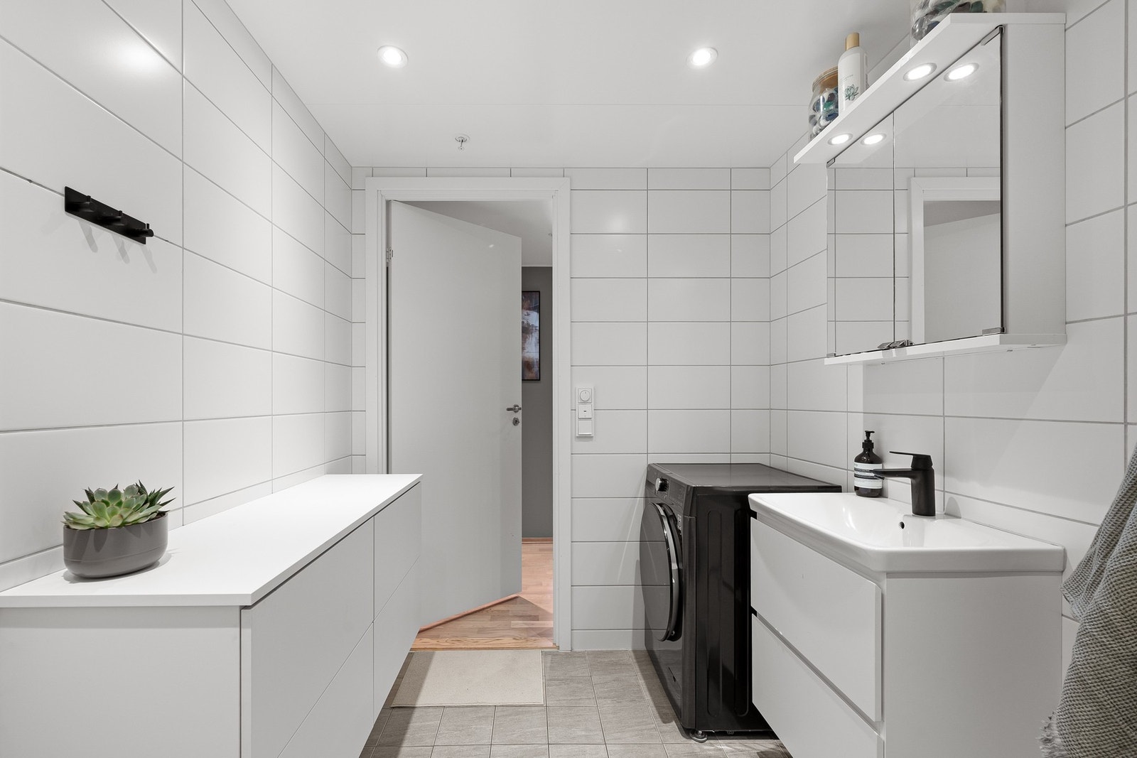 Badet er utstyrt med heldekkende servant, dusj med innfellbare glassvegger, speilskap med lys og vegghengt toalett med skjult sisterne. Galleribilde