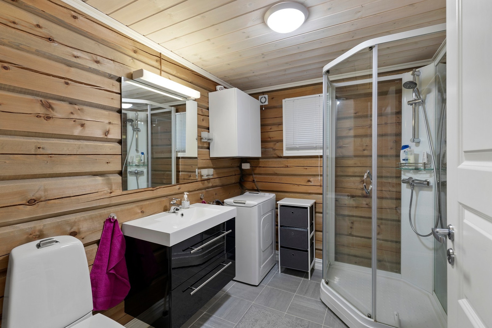 Badet har fliser på gulv og er utstyrt med varmekabler i gulv, dusjkabinett, toalett og lekker innredning i svart høyglans med servant, speil og belysning. Galleribilde