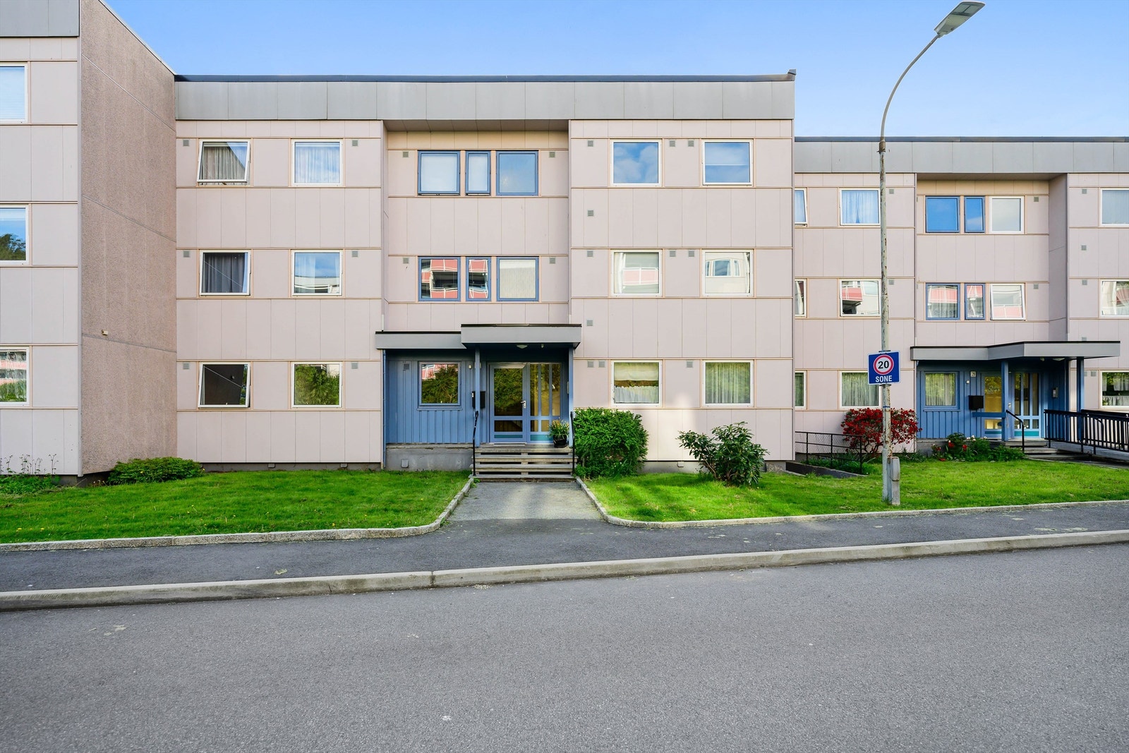 Inngangspartiet har grønne plener, beplanting og asfaltert gangvei. Galleribilde