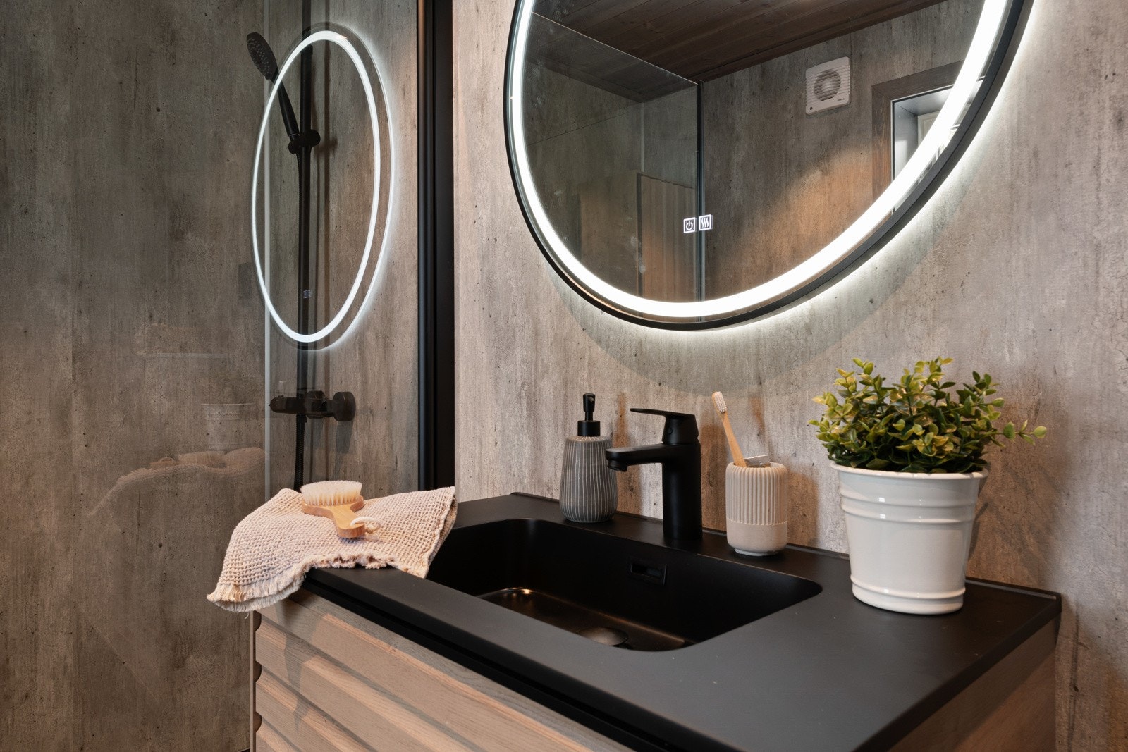 Innredningen består av en heldekkende, sort servant på skuffeseksjon med lamellfronter i eik og et rundt speil med rammebelysning Galleribilde