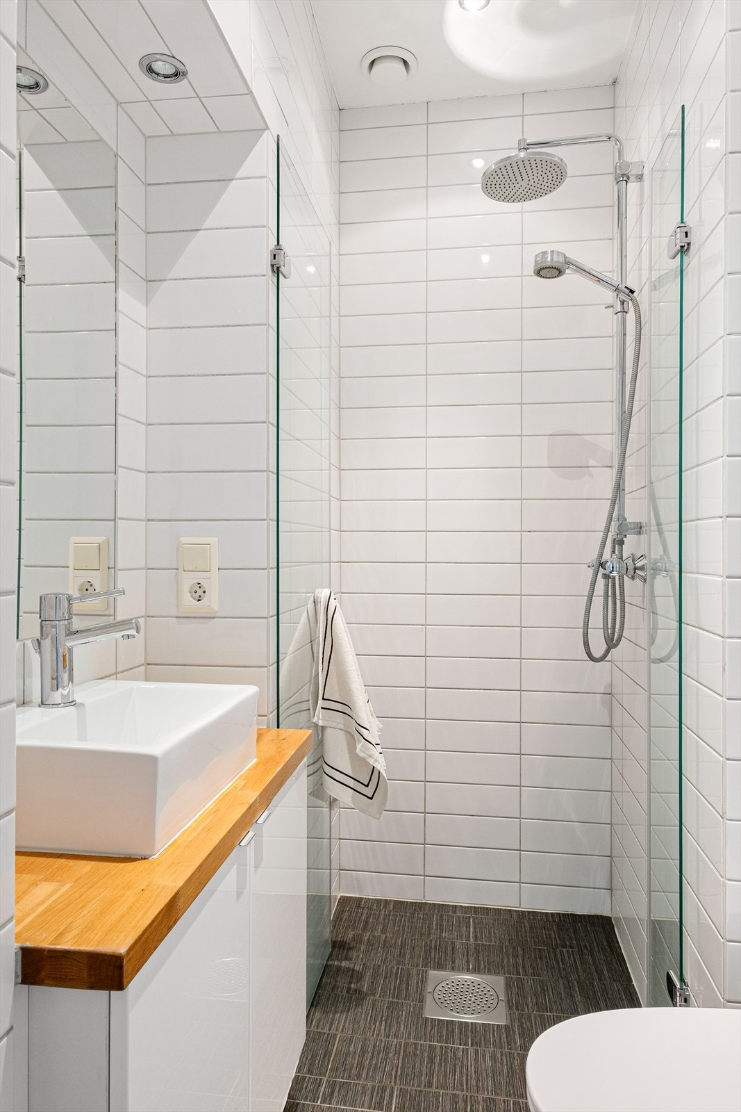 Baderommet er innredet med vegghengt klosett, servant plassert på innredning og dusjhjørne med svingbare glassdører. Galleribilde