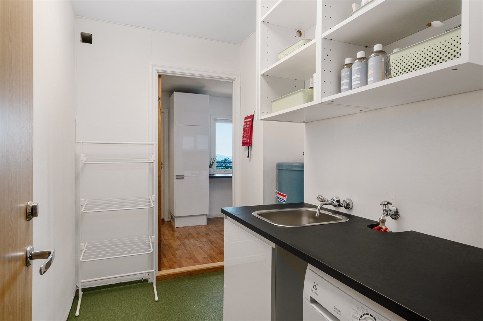 Fra kjøkkenet er det dør til leilighetens vaskerom. Her er det skyllekar og opplegg for vaskemaskin. Varmtvannstank er plassert på vaskerom. Galleribilde