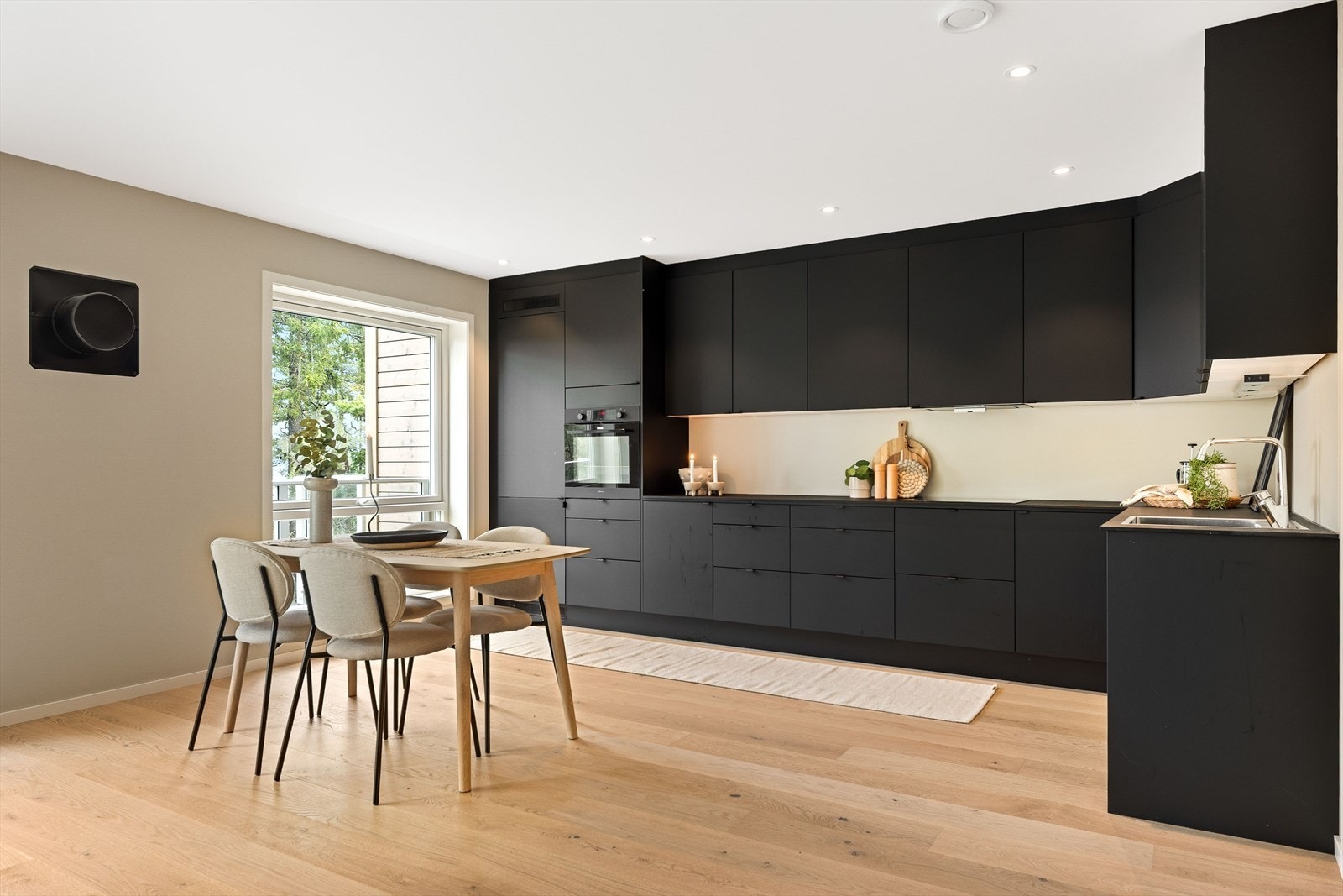 Delikat kjøkkendel i åpen løsning, med takhøy kjøkkeninnredning type Systemkjøkken. Innredningen er stilig og mørk, med integrerte hvitevarer. Galleribilde