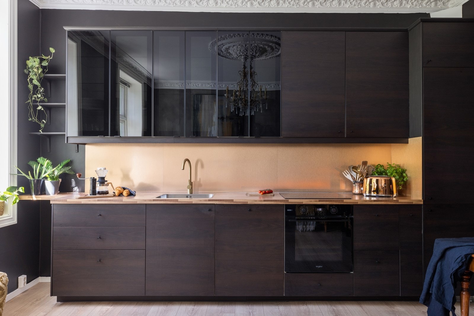 Kjøkkeninnredning med tremønstret fronter, laminat benkeplate, planlimt oppvaskkum i stål og metallplate over benk. Galleribilde