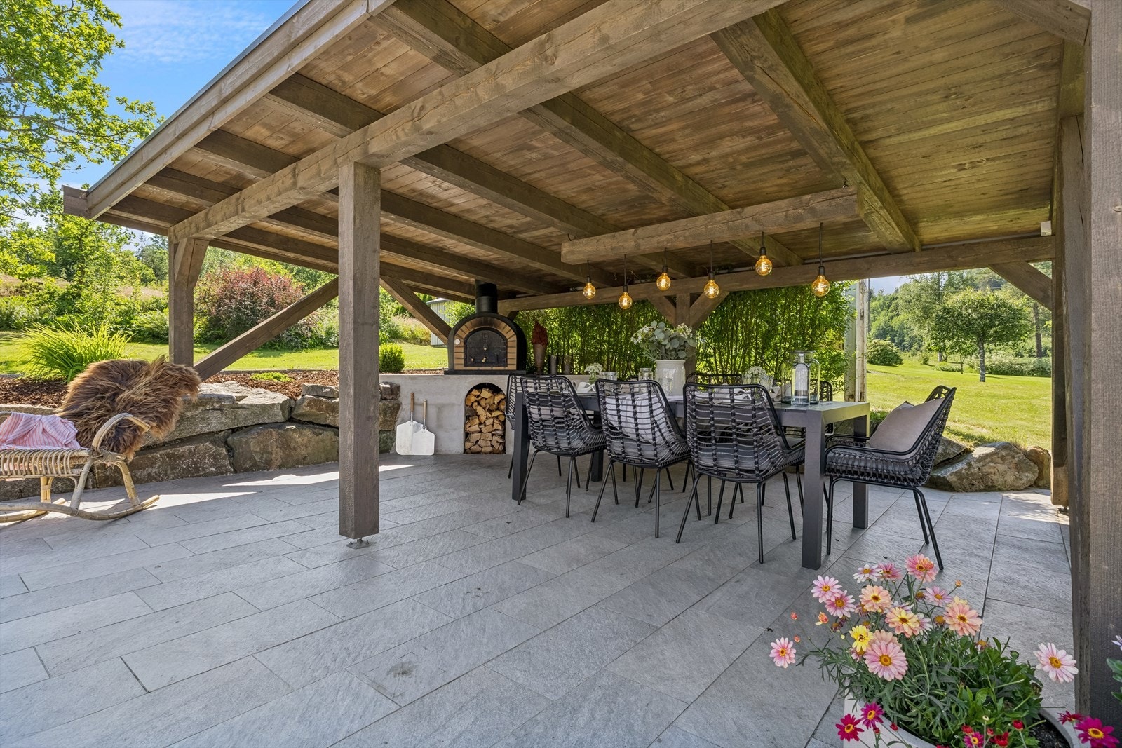 Uteplattingen ved inngangspartiet har flislagt gulv og pergola med plassbygd peis/pizzaovn Galleribilde