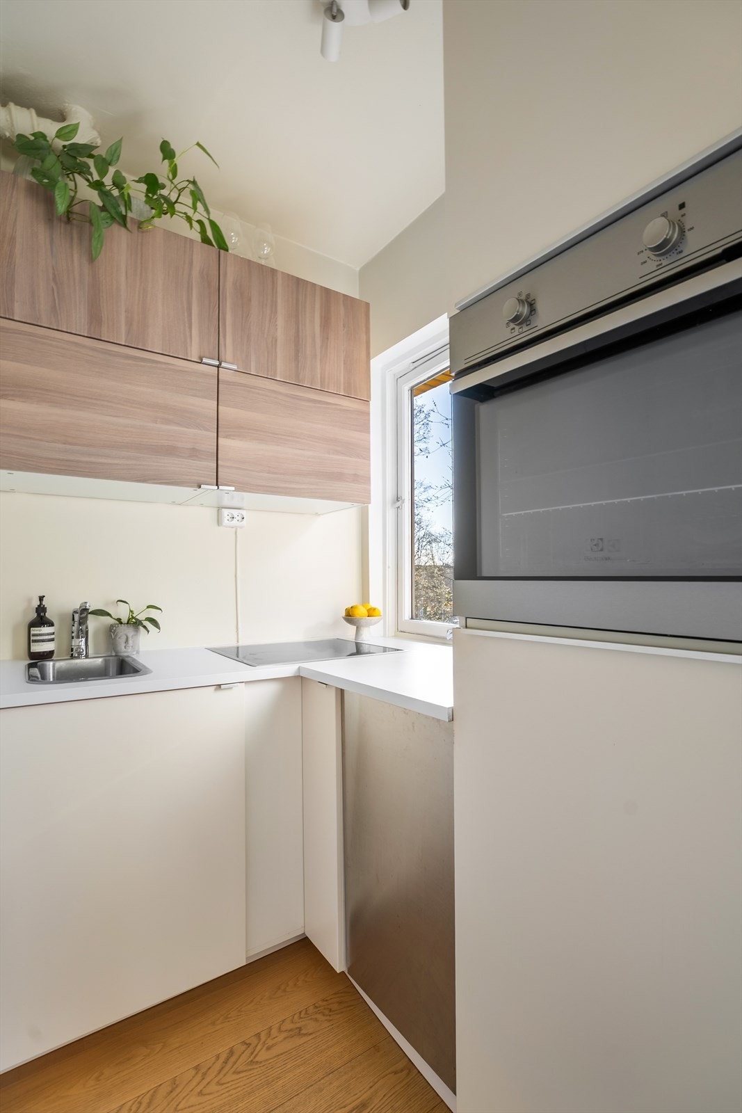 Koselig kjøkken med slettefronter og benkeplate av laminat med nedfelt oppvaskkum med ett-greps kran. Kjøkkenet er utstyrt integrert komfyr, kjøleskap i høyskap og oppvaskmaskin i benk. Galleribilde