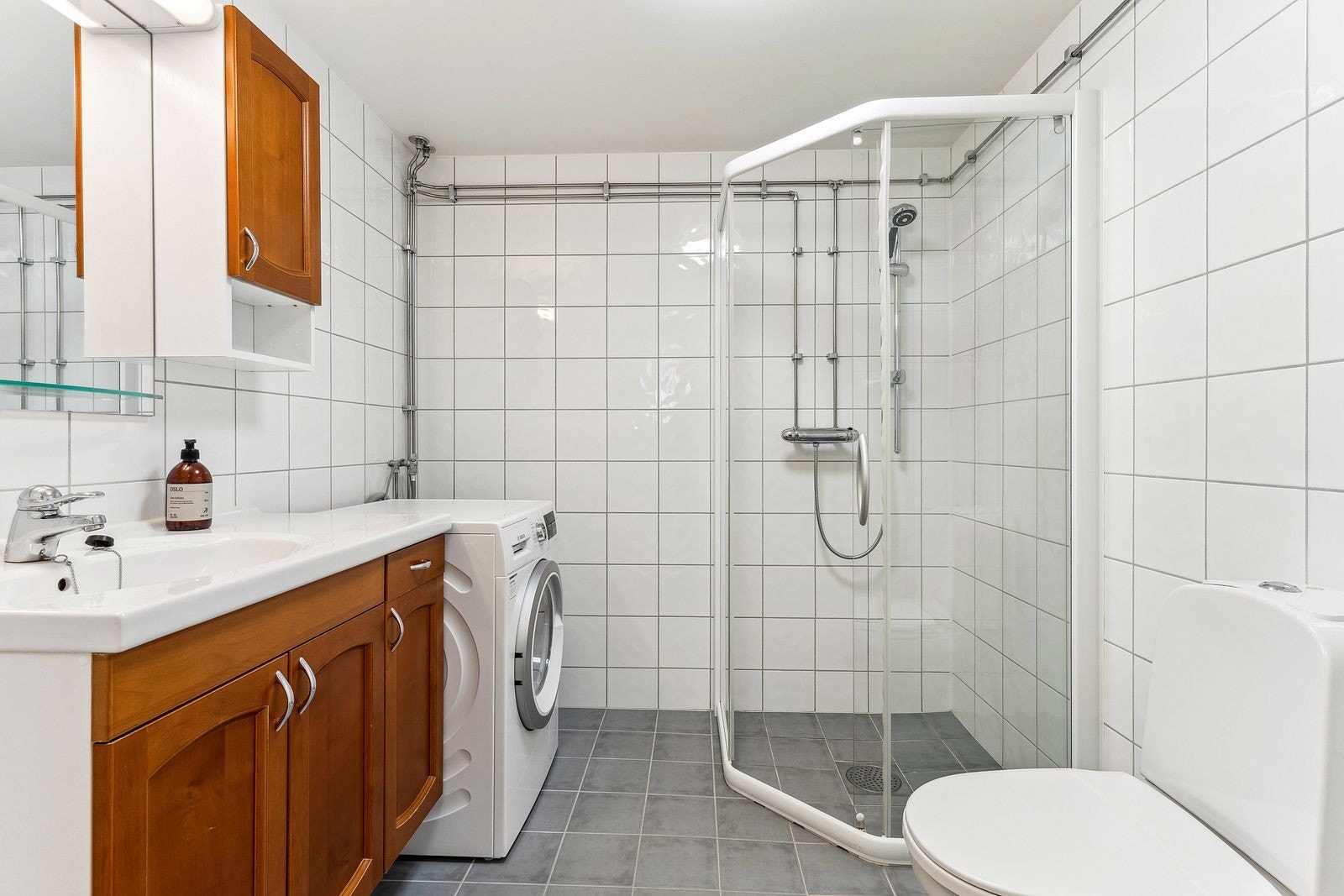 Lyst bad med med dusjhjørne, servant, WC, og opplegg for vaskemaskin. Galleribilde