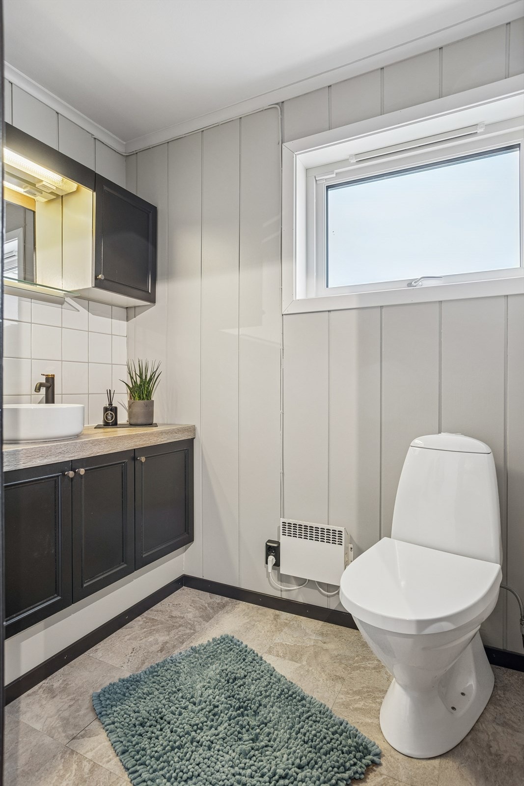 WC har panel og fliser på veggene, samt malt tak. Her er det montert ny servant på et eldre møbel, og gulvet har vinylfliser. Galleribilde