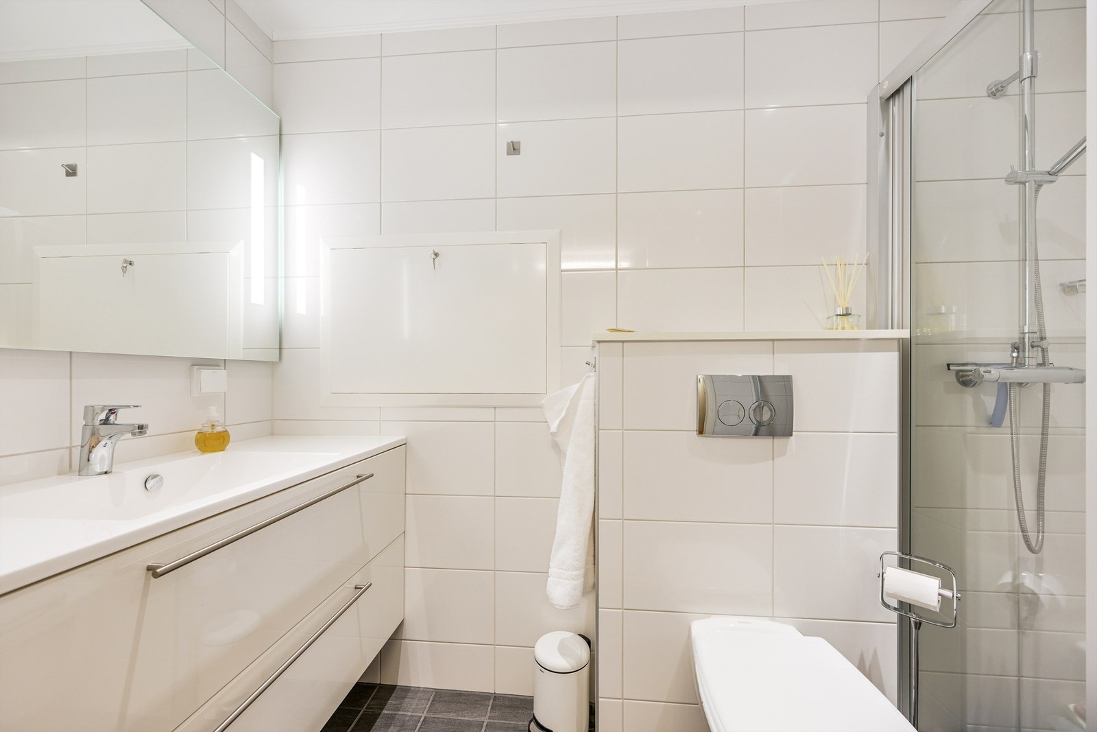 Lyst bad med varmekabler på gulvet. Innredet med nedfelt servant, dusjvegg i glass montert med skinne oppe og nede og veggmontert toalett. Galleribilde