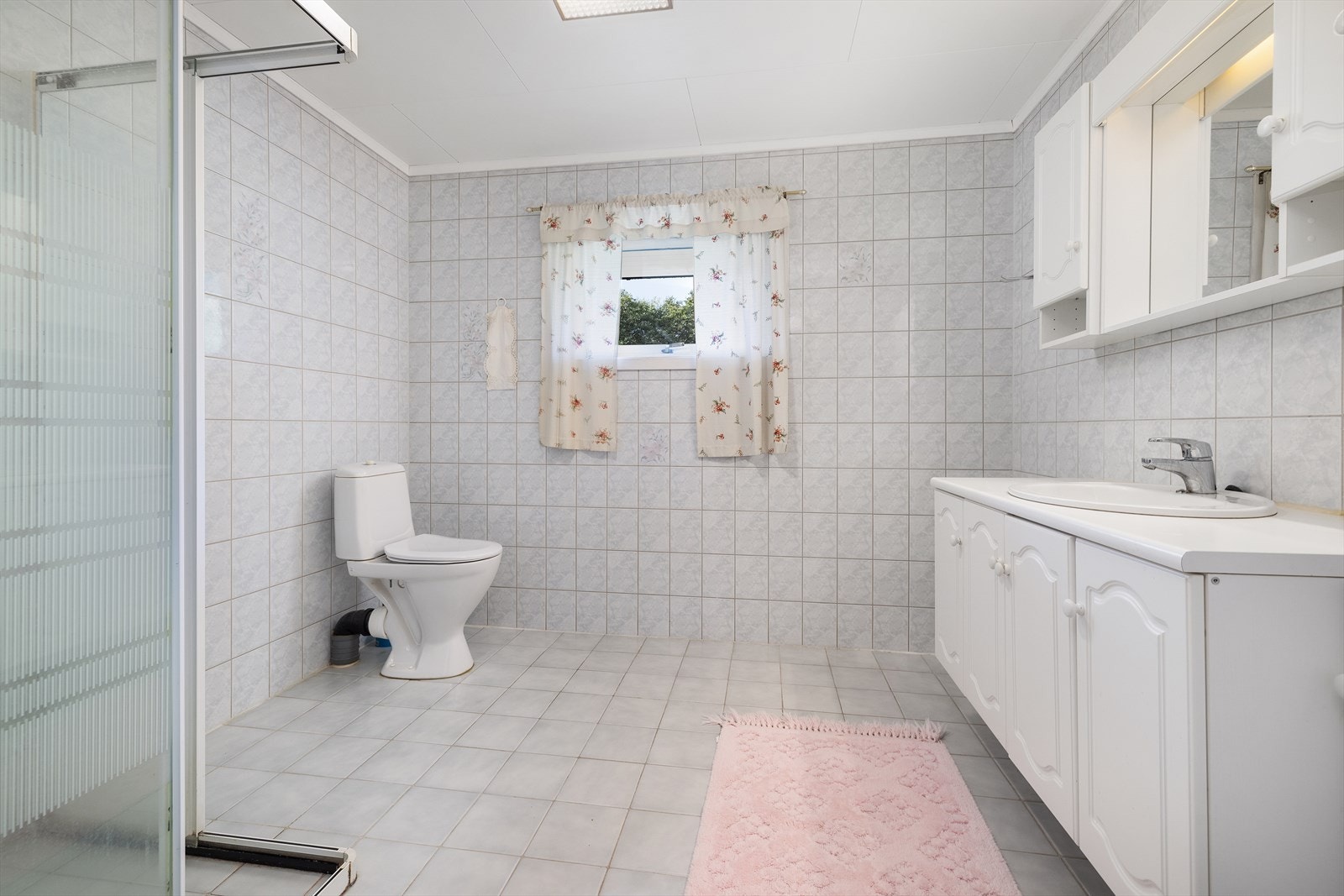 Det er montert dusjvegger med sokkel på gulv, frittstående toalett og servantinnredning. Galleribilde