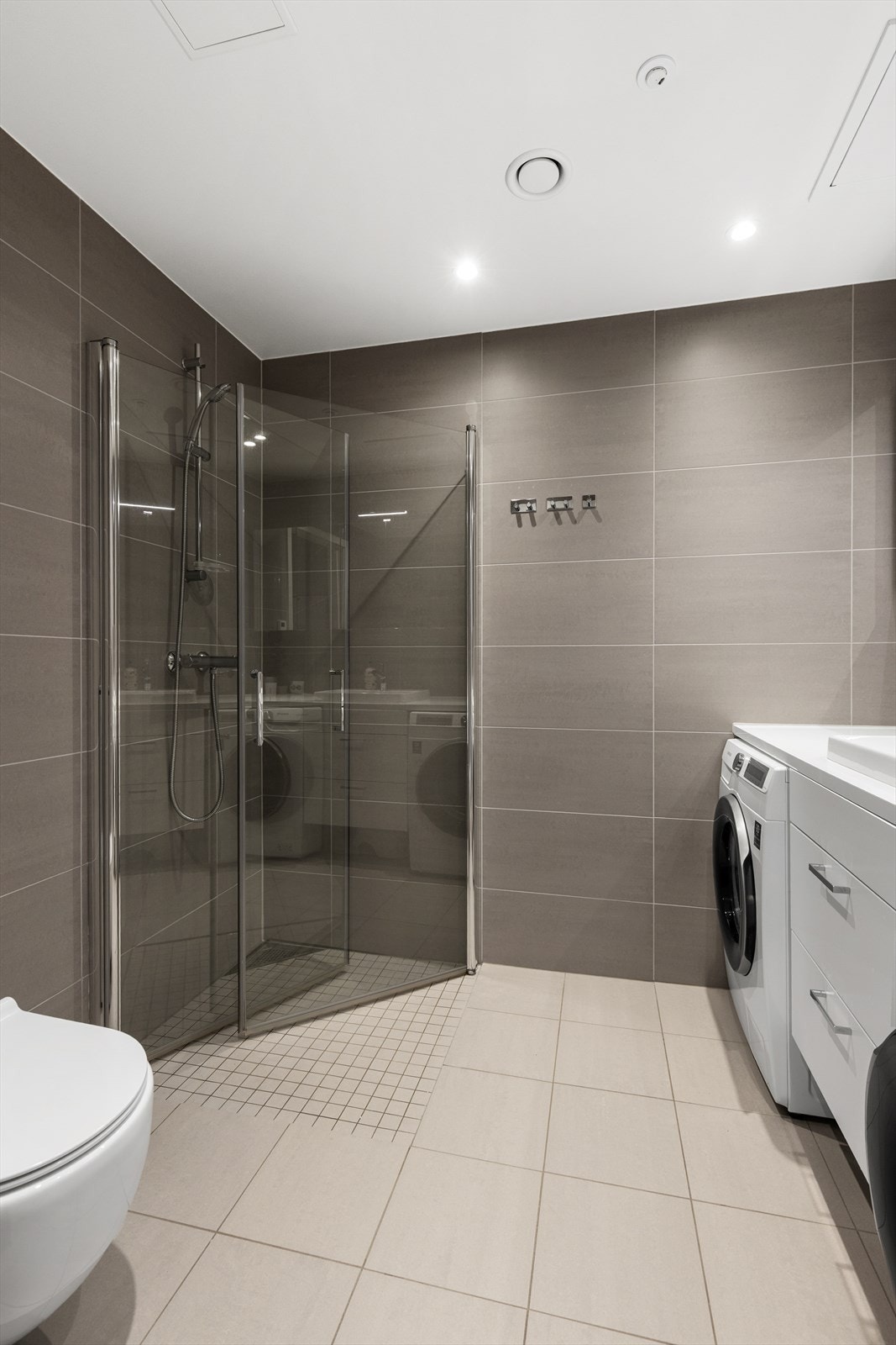 Badet er innredet med vegghengt klosett, servant nedfelt i benkeplate og dusjhjørne med svingbare glassdører. Galleribilde