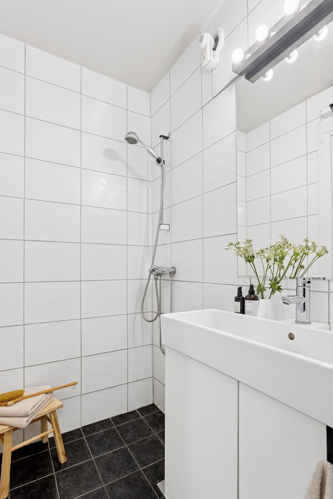 Innredningen består av et hvitt servantskap med glatte fronter og heldekkende servant, speil, toalett og et åpent dusjhjørne. Galleribilde