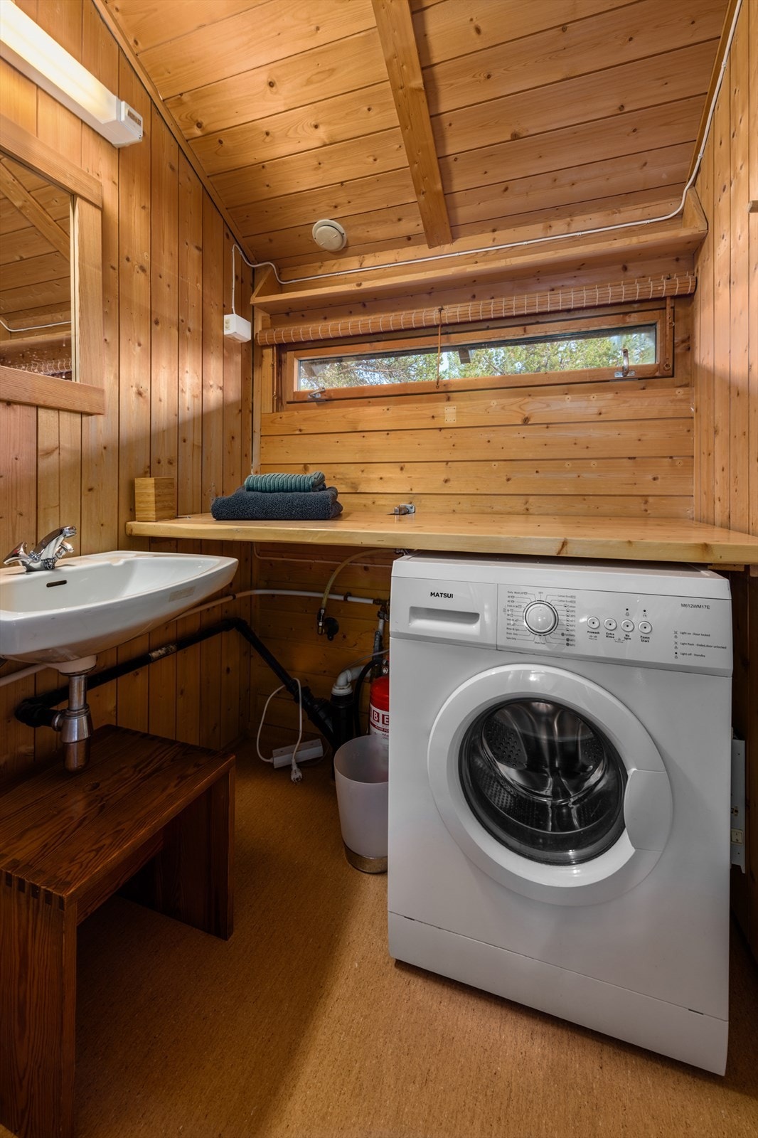 Belegg på gulv og trepanel på vegger. Badet har benkeplate, nedfelt skyllekum, håndvask og dusjkabinett. Opplegg for vaskemaskin. Varmtvannsbereder ca. 120 L, 1979 modell plassert på hylle over dusjkabinett. Galleribilde