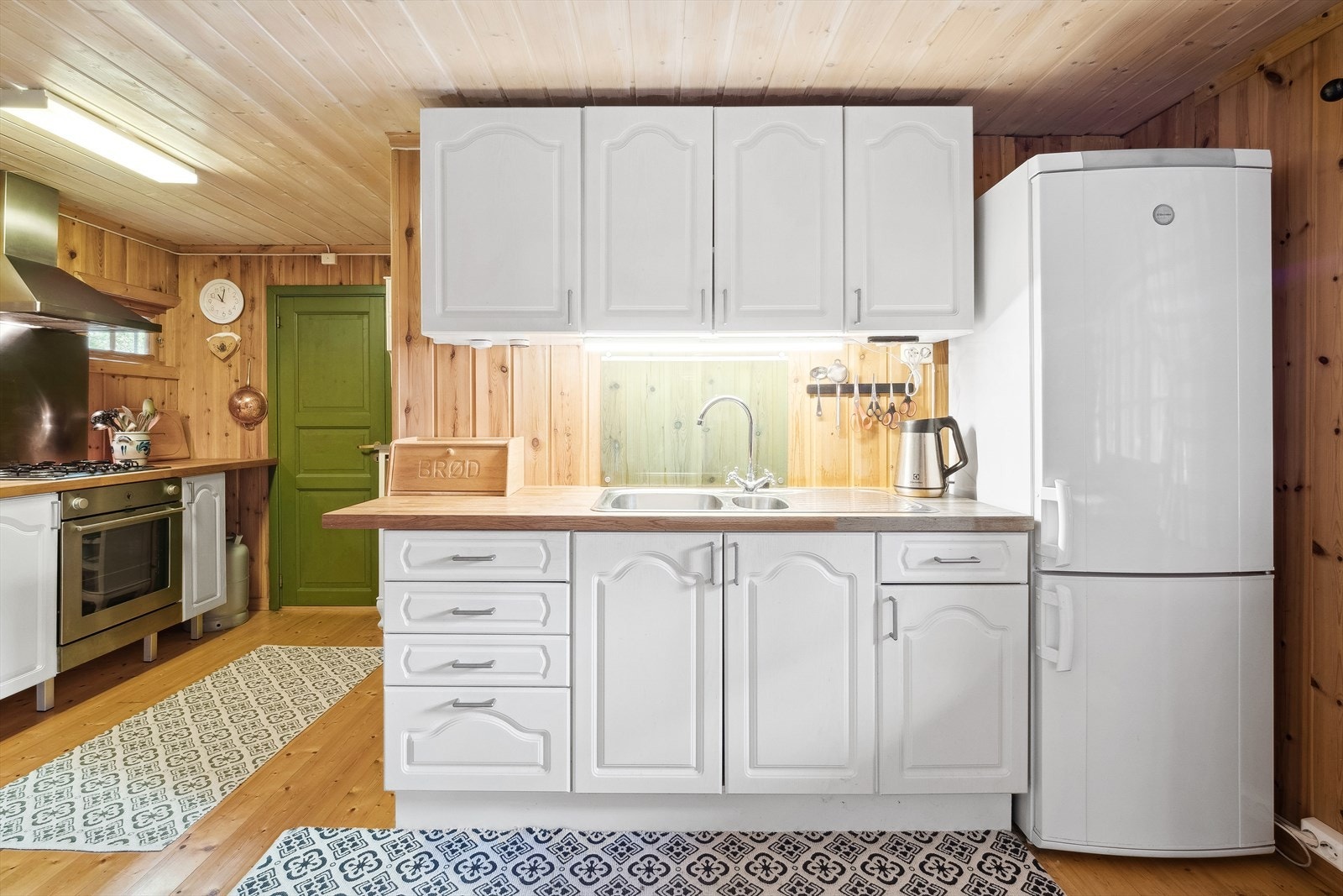 Innredningen i rommet er utført med laminerte skrog, profilerte fronter, heltre benkeplate m/kjøkkenkum og glass/plastplater og metallplate over deler av benkeplaten. Galleribilde