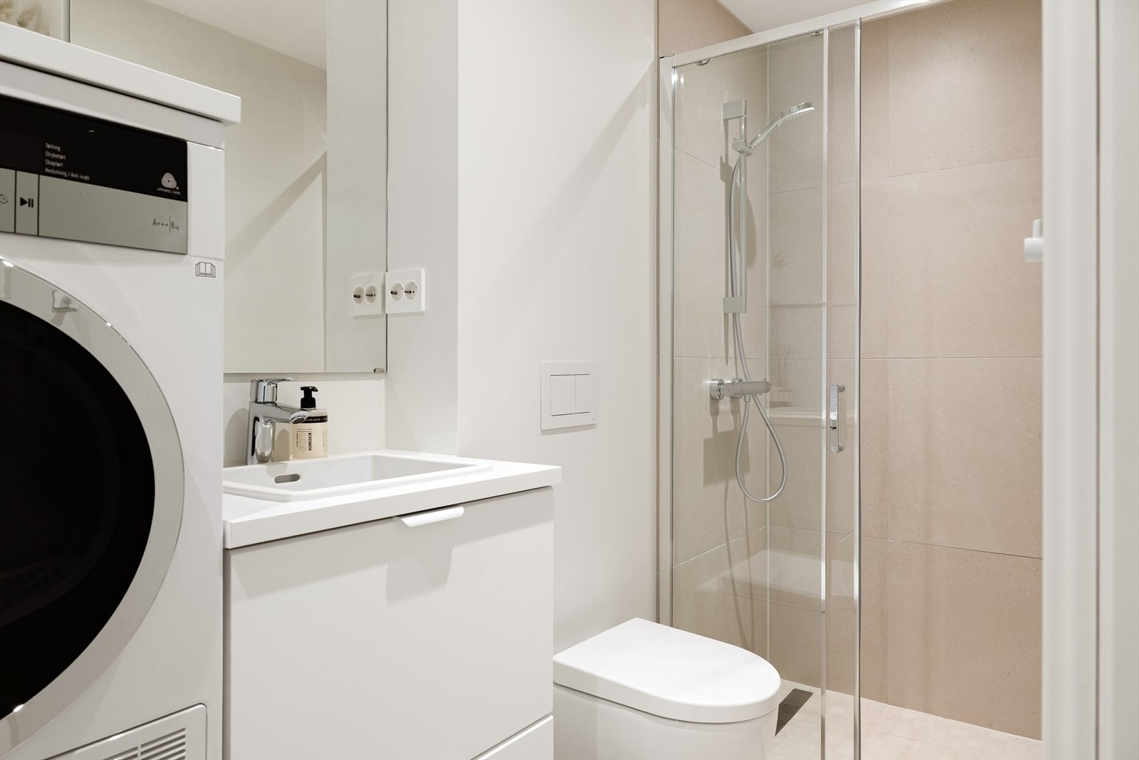 Badet er innredet med vegghengt toalett, dusjhjørne og opplegg for vaskemaskin og tørketrommel. Galleribilde