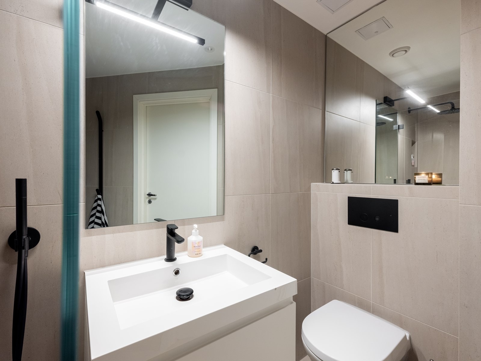 Badet er innredet med nedfelt servant, overhengende speil med belysning, vegghengt toalett, og dusjhjørne med glassvegger. Galleribilde