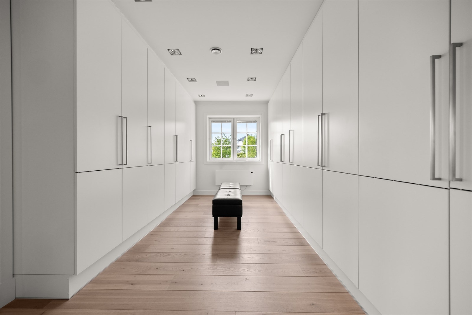 Walk-in med svært romslig garderobeløsning som har takhøy skapinnredning i hvit samt glatt utførelse Galleribilde