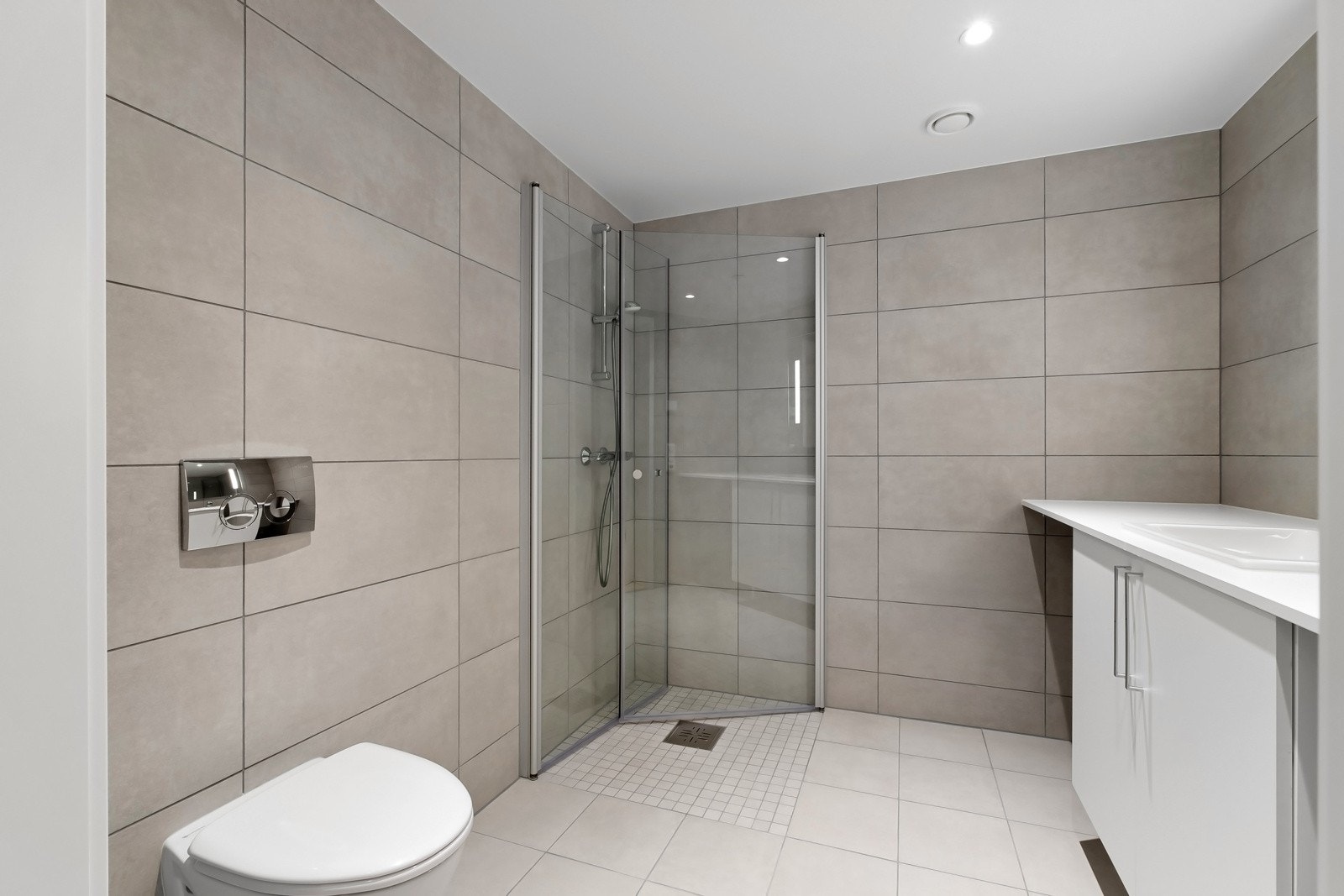 Delikat flislagt bad med vegghengt toalett, dusjsone med innfellbare dører samt servant med skapinnredning. Galleribilde