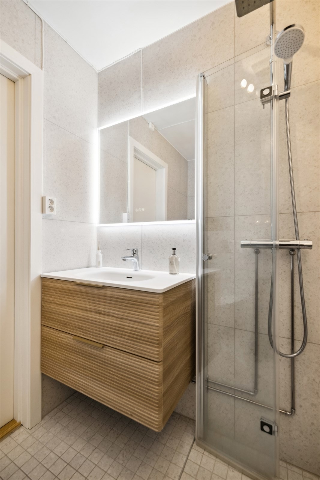 Flislagt bad med gulvvarme, servant med innredning, vegghengt toalett og en dusjløsning med dusjvegg som kan felles inn Galleribilde