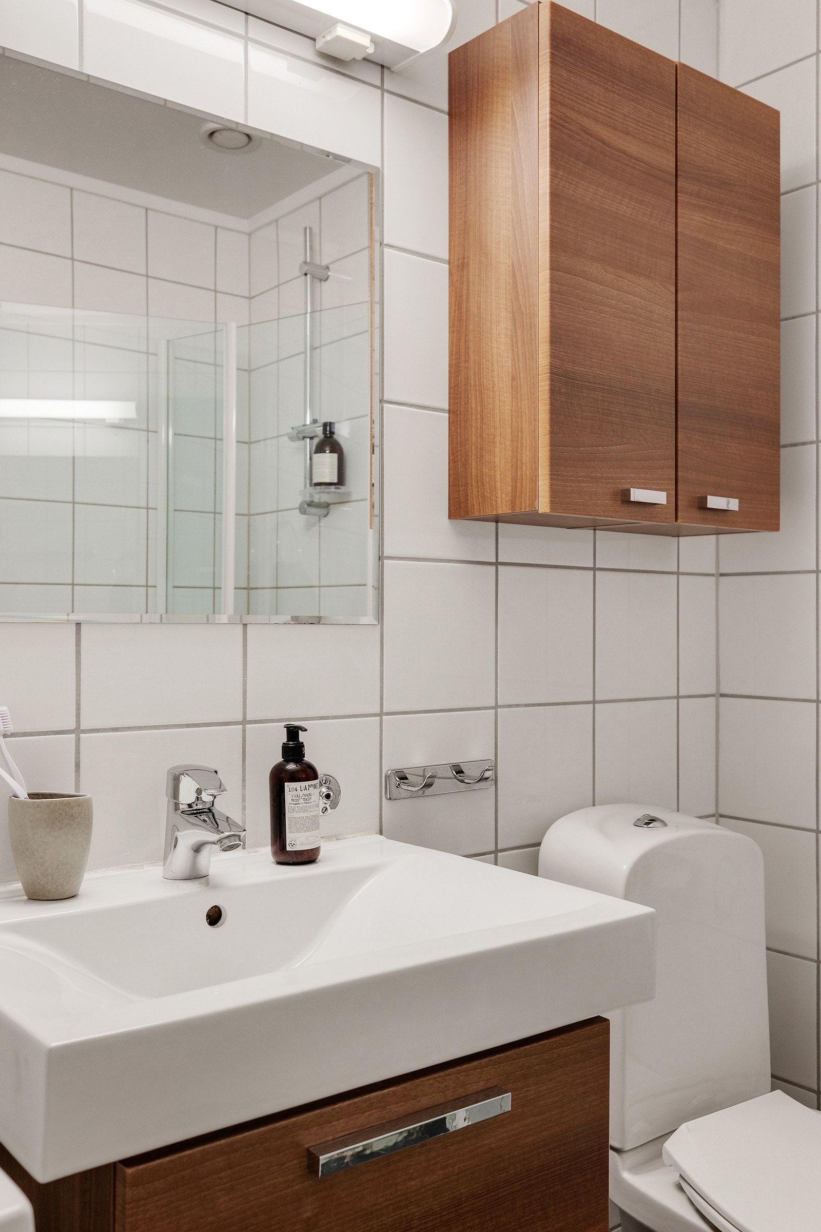 Badet inneholder vegghengt innredning med skuffer og heldekkende servant, speil med overbelysning, vegghengt skap, gulvmontert wc og dusjhjørne med innfellbare dører i glass. Galleribilde