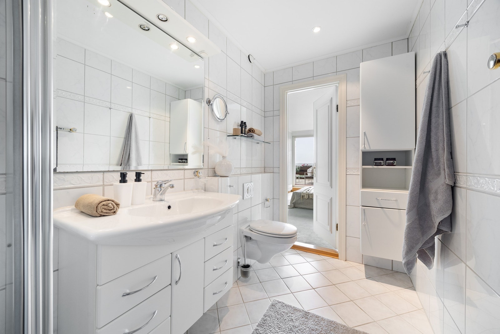 Hovedbadet med inngang fra soverom har vegghenht toalett, servant med skap, dusj og vegghengt skaprekke. Galleribilde