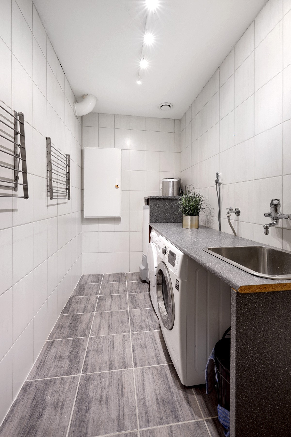 Romslig vaskerom med fastmonterte tørkestativ, vask, varmtvannsbereder og opplegg for vaskemaskin Galleribilde