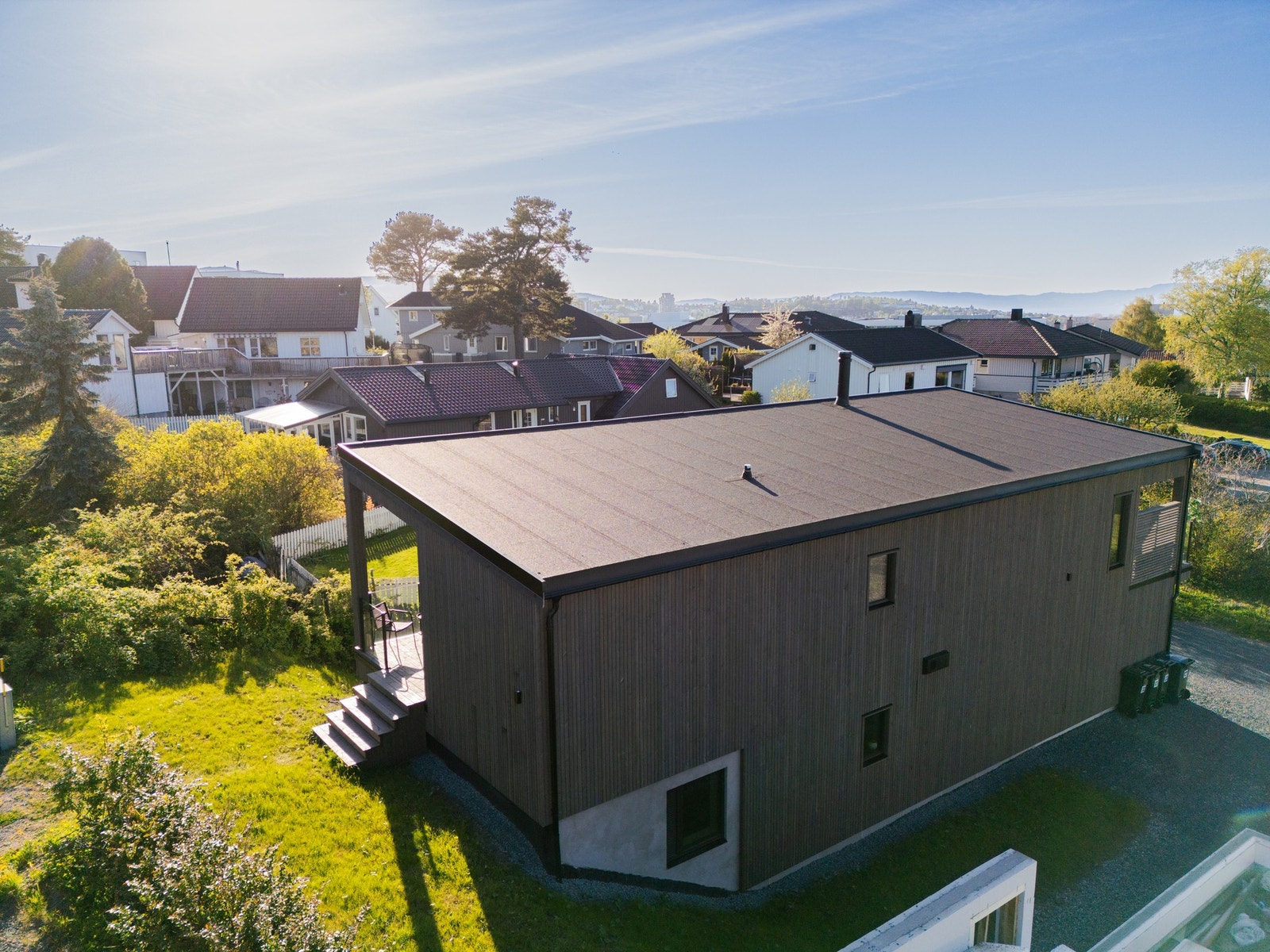 Fasadebilde med plen på sørsiden av boligen. Nede til høyre skimtes en av de to øvrige boligene som skal oppføres på tomta. Galleribilde