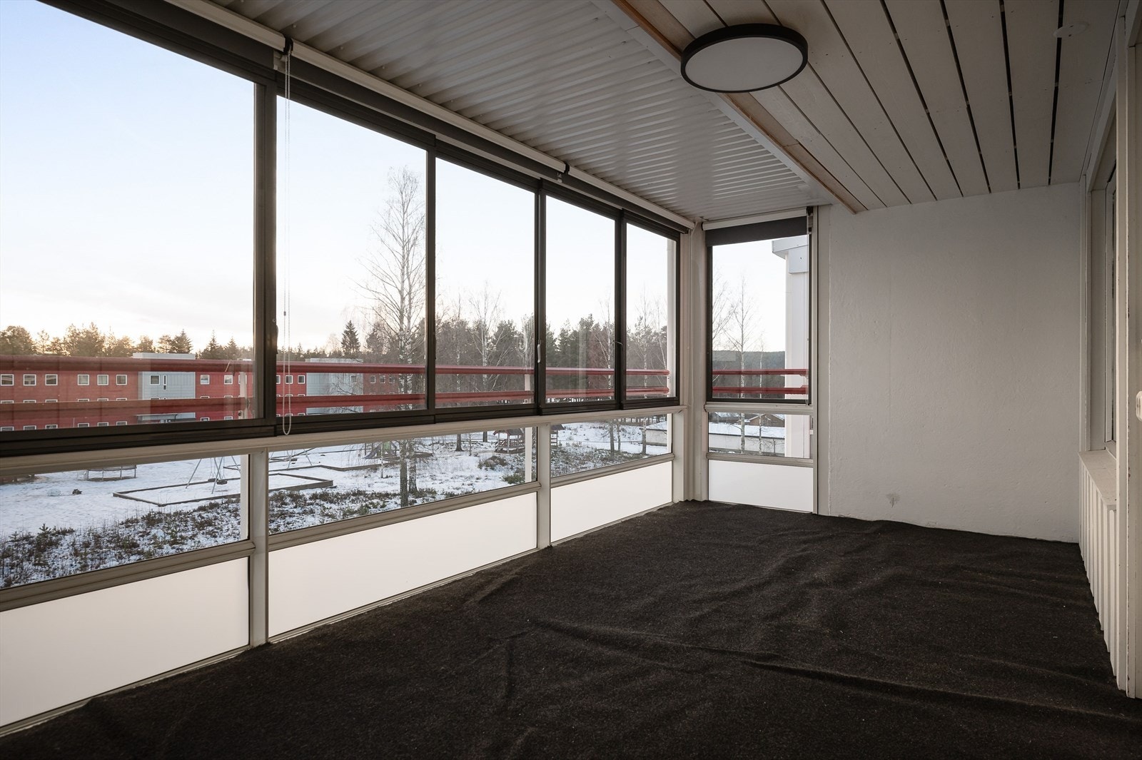 Innglasset balkong med nålefiltdekke på gulvet og utsikt over borettslagets fellesarealer. Galleribilde