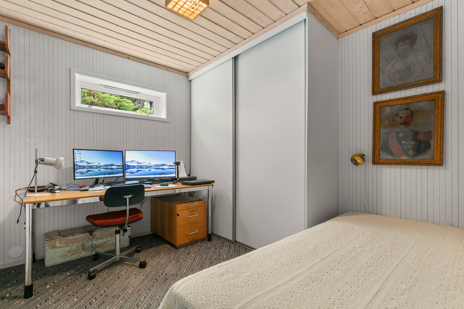 Et kontor i underetasjen er innredet med kontorpult, skyvedørsgarderobe og seng Galleribilde