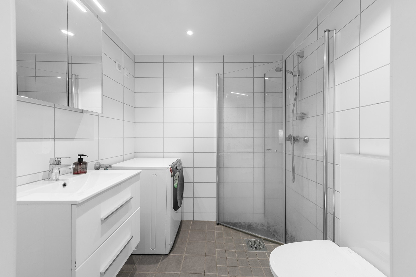 Romslig flislagt bad med opplegg for vaskemaskin, vegghengt WC og innfellbare dusjvegger. Galleribilde