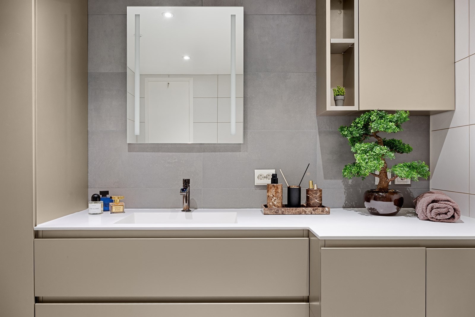 Over benken er det speil med integrert lys, samt høyskap og veggskap i matchende stil. Badet har vegghengt toalett, dusjhjørne med svingbare glassdører og skjult opplegg for vaskemaskin i innredningen - smart og diskret Galleribilde