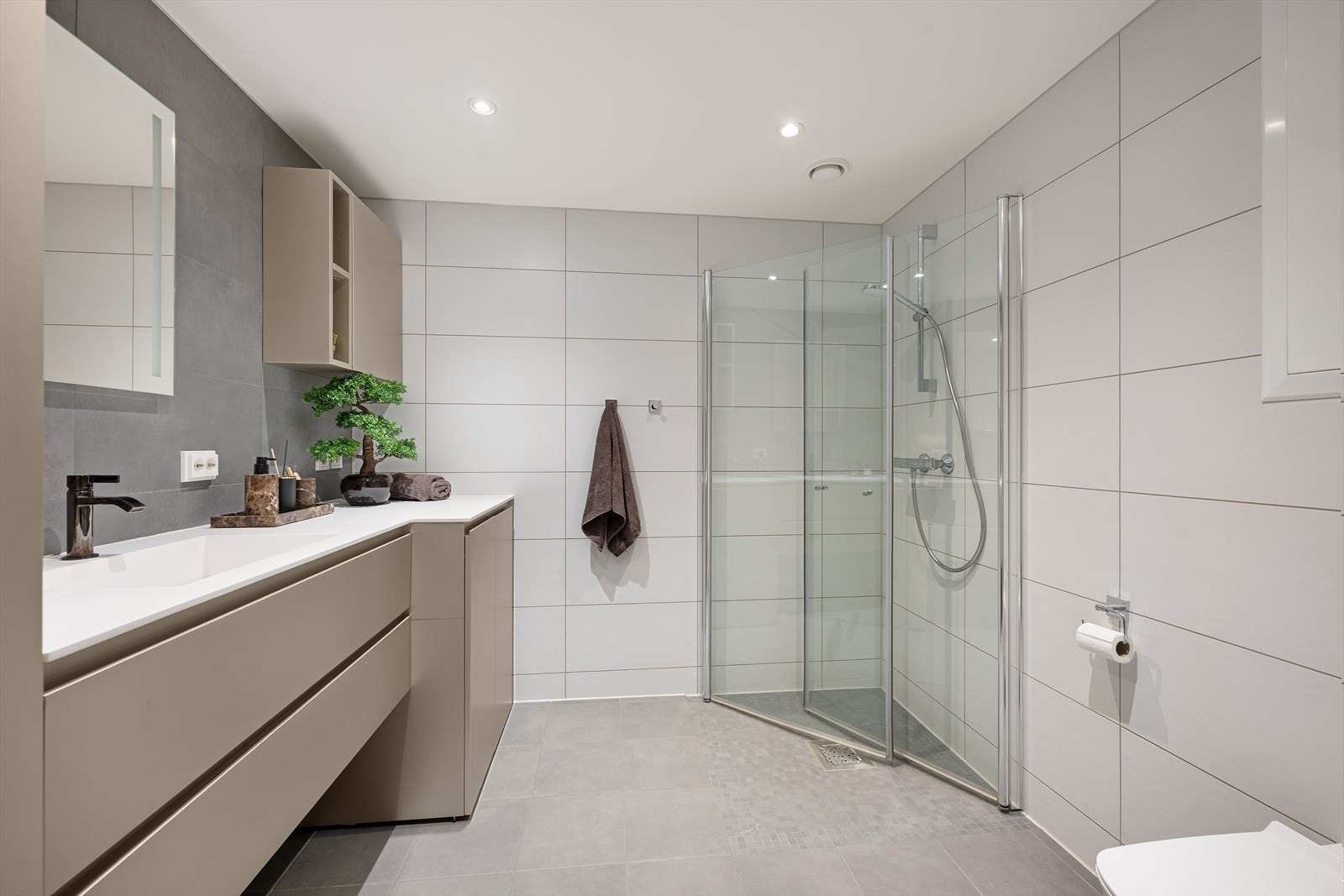 Leiligheten har to pene, flislagte baderom med behagelig gulvvarme og downlights i himling - Badet ved entré ble nylig oppgradert med nye baderomsmøbler og har en moderne innredning med beige fronter og en lang benkeplate i Corian med nedfelt servant Galleribilde