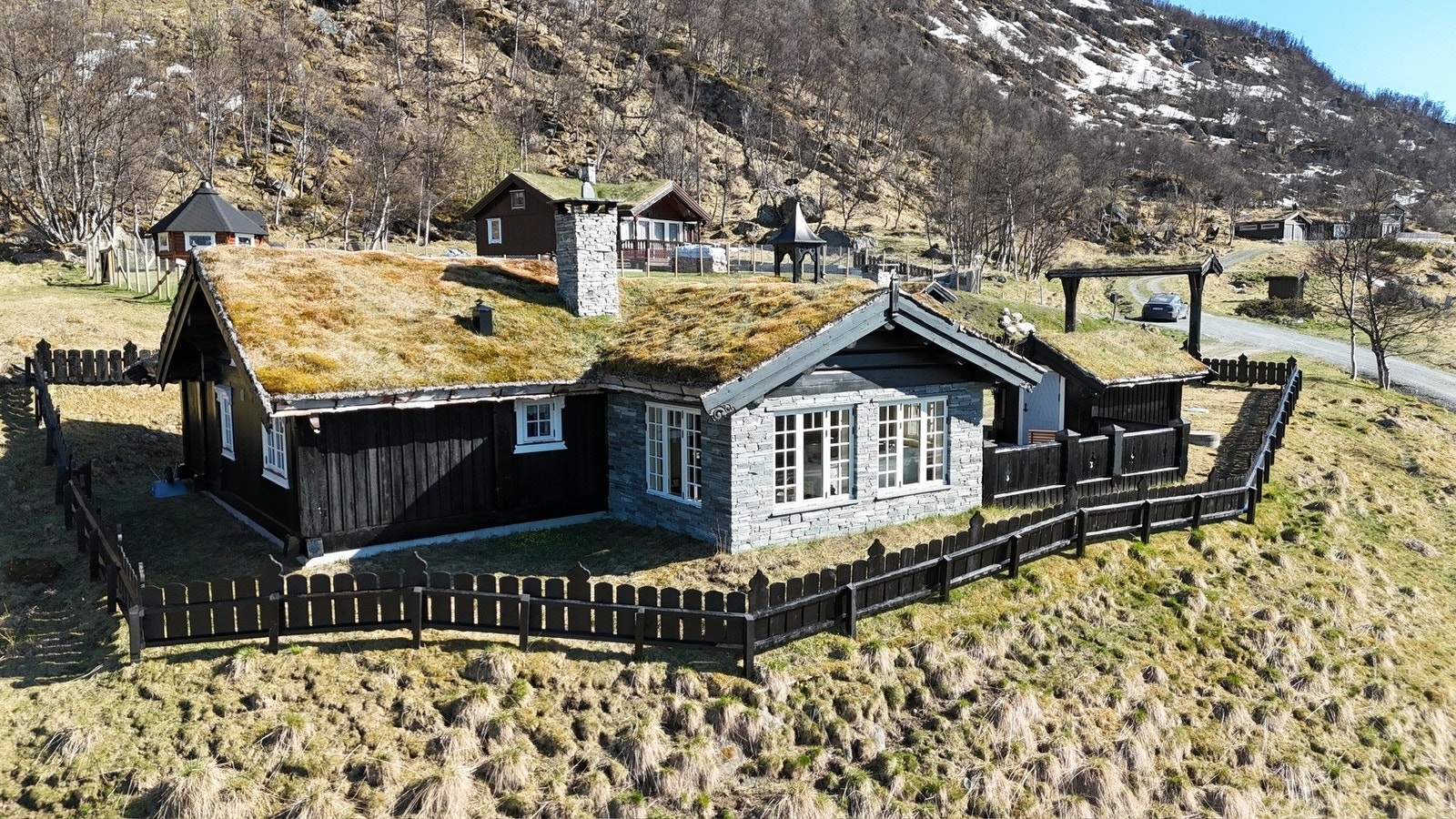 Hytta er perfekt tilpasset tomten og landskapet, med tradisjonelt torvtak, mørk kledning og delvis skiferstein. Galleribilde