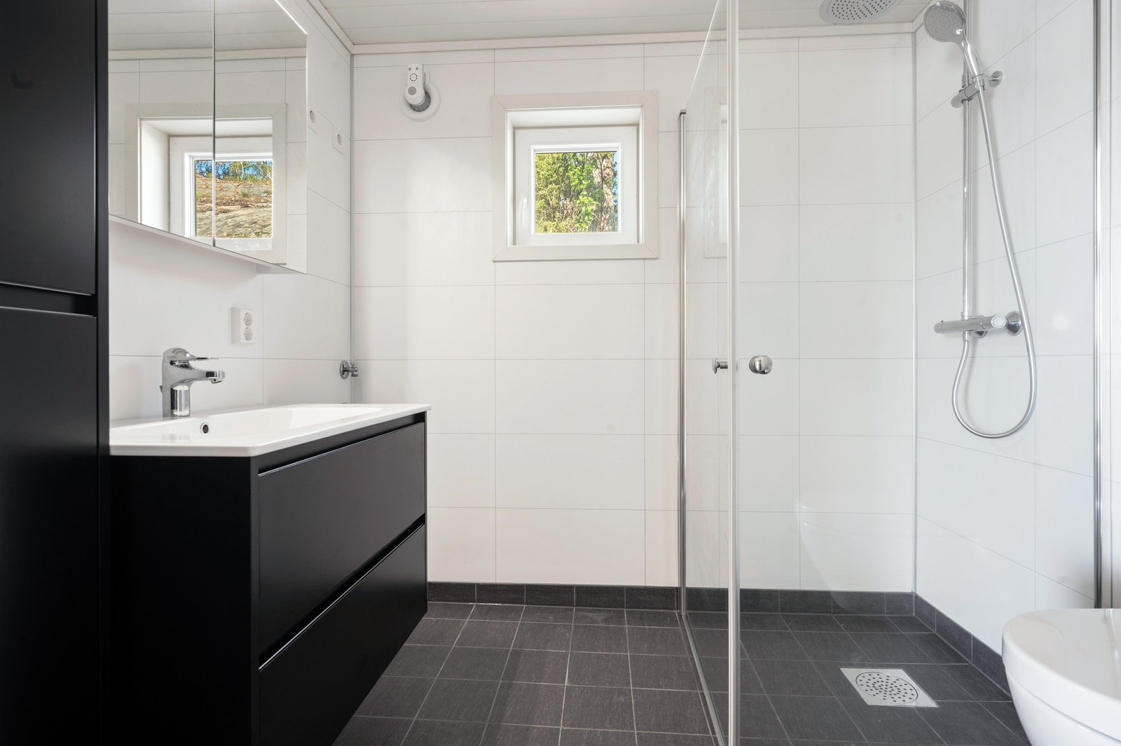 Badet har veggfestet toalett, dusjhjørne, innredning med servant og opplegg for vaskemaskin. Galleribilde