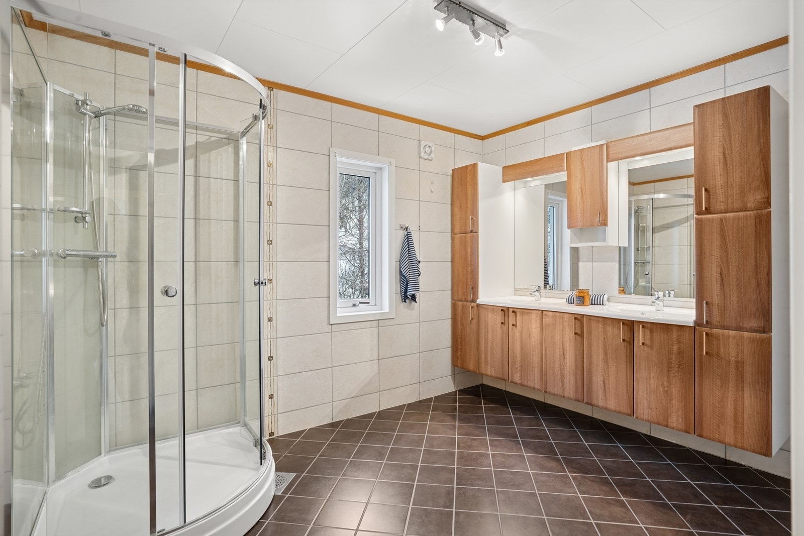 Badet er romslig og har stor innredning med dobbel vask og 2 speil. Dusjkabinett. Fliser på gulv og vegg. Varmekabler Galleribilde